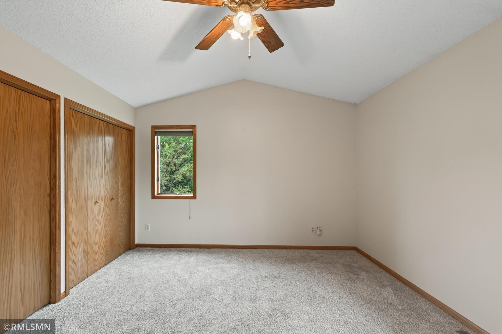 Empty bedroom with a wooden closet, small window, carpet, and ceiling fan.