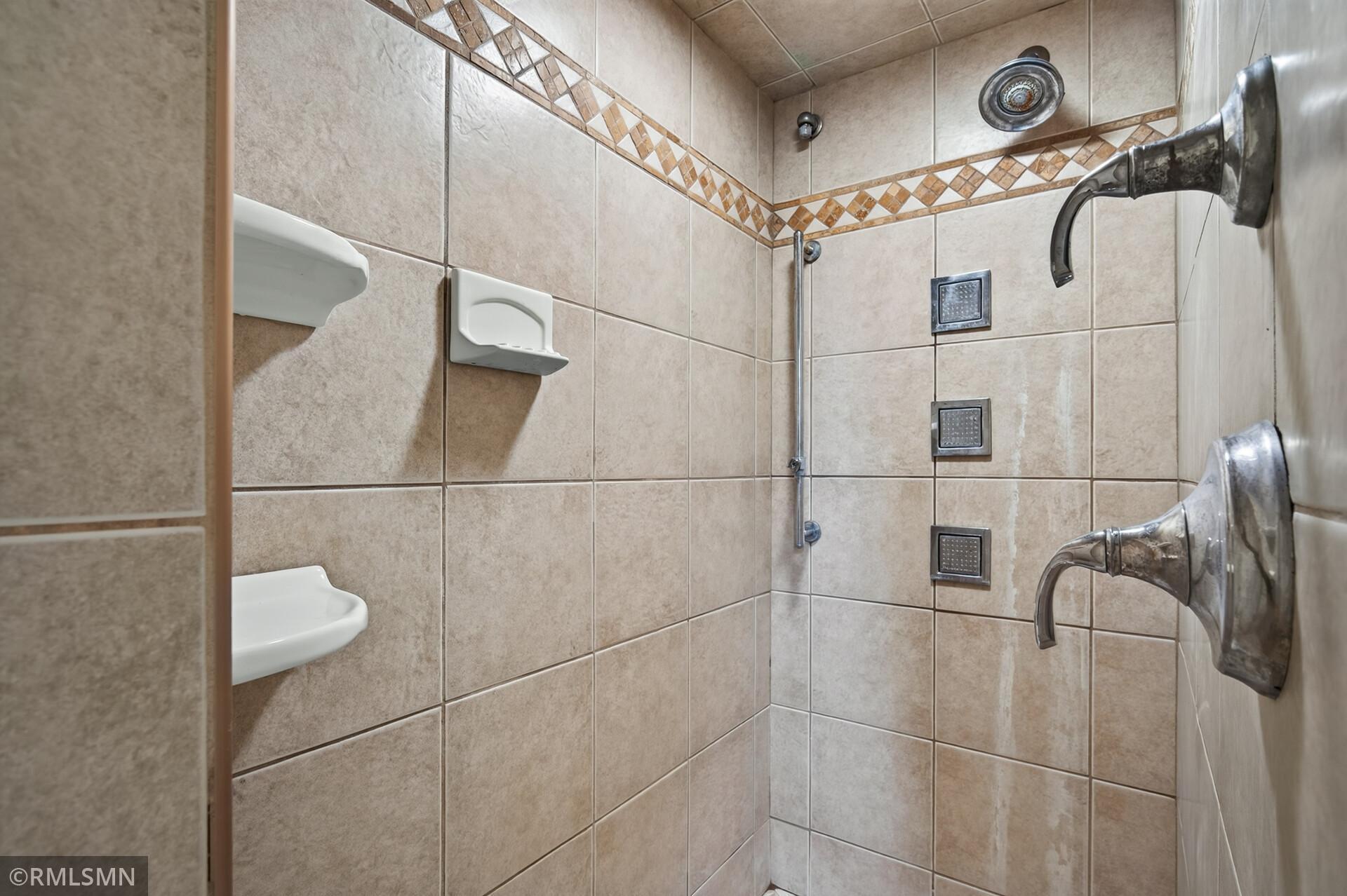 Tiled bathroom shower with a mosaic border, multiple shower sprays, and built-in soap dishes.