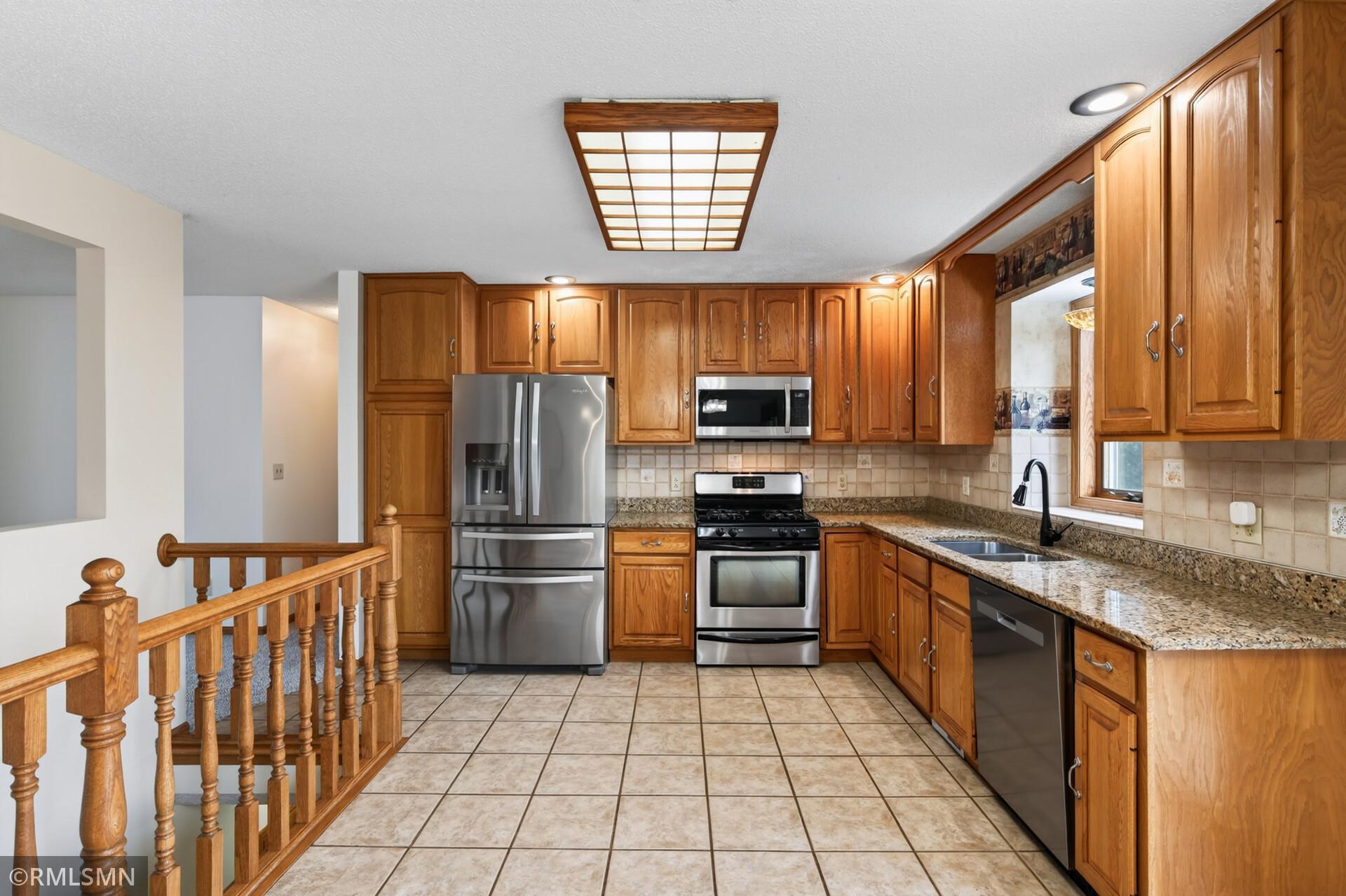 Kitchen with extensive wood cabinetry, granite counters, stainless steel refrigerator, and tiled floor.