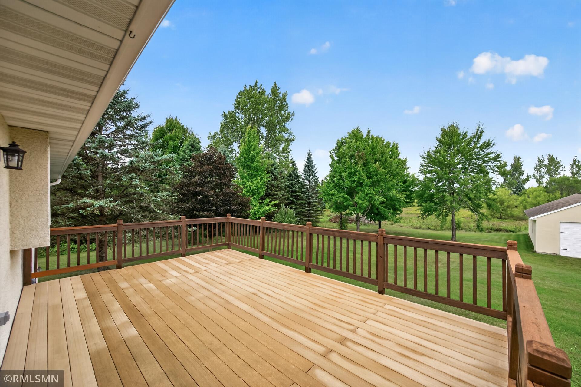Wood deck with brown railings overlooking a leafy yard and detached garage
