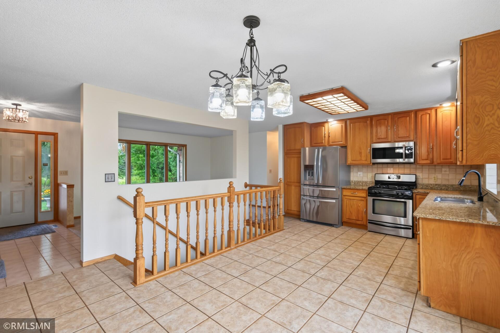 Kitchen with wood cabinets, stainless steel appliances, granite counters, and an open stairwell railing.