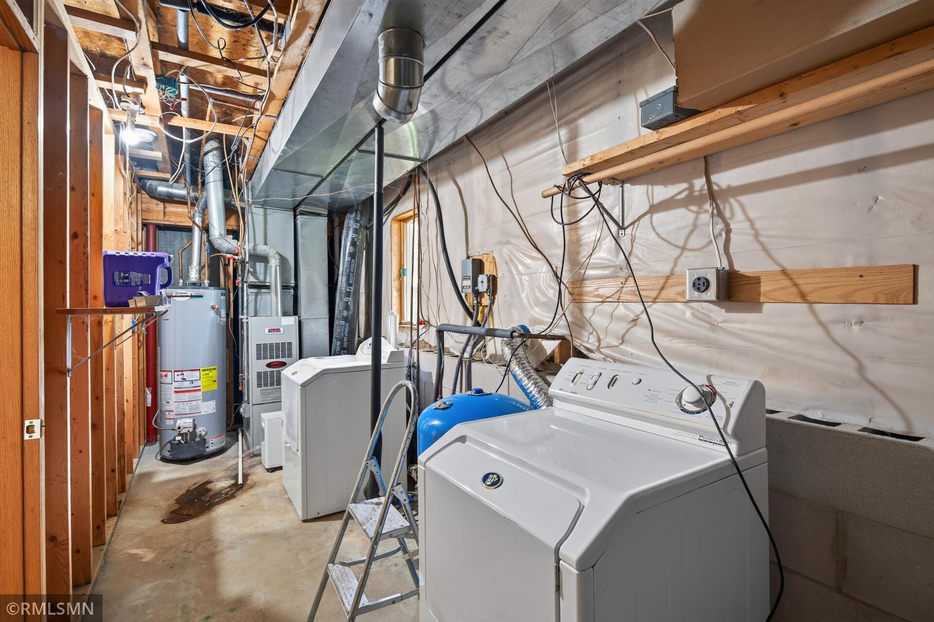 Basement laundry and utility room with washer, dryer, water heater, and exposed framing.
