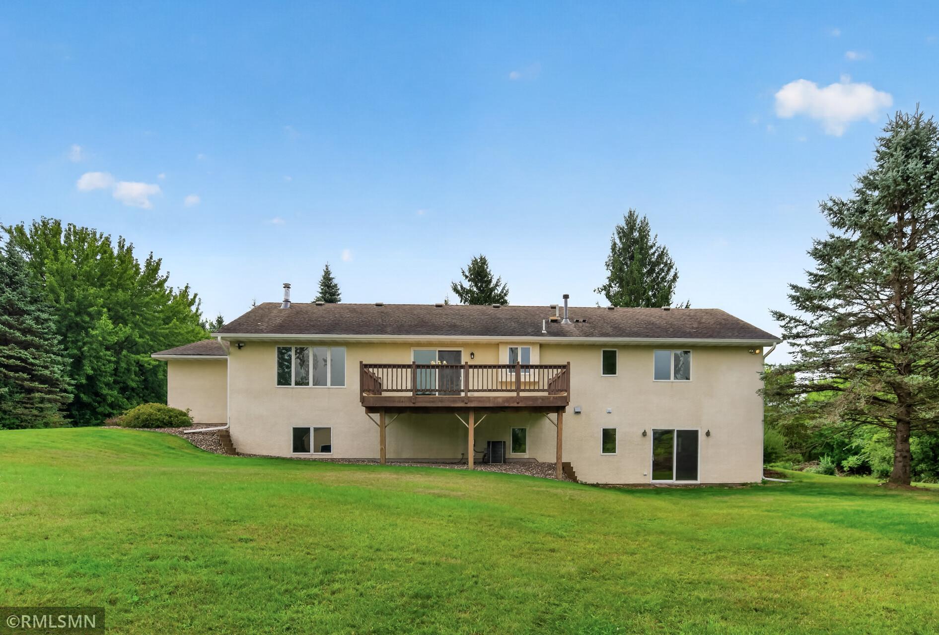Rear of a beige home with a raised wooden deck, walkout lower level, and broad lawn.