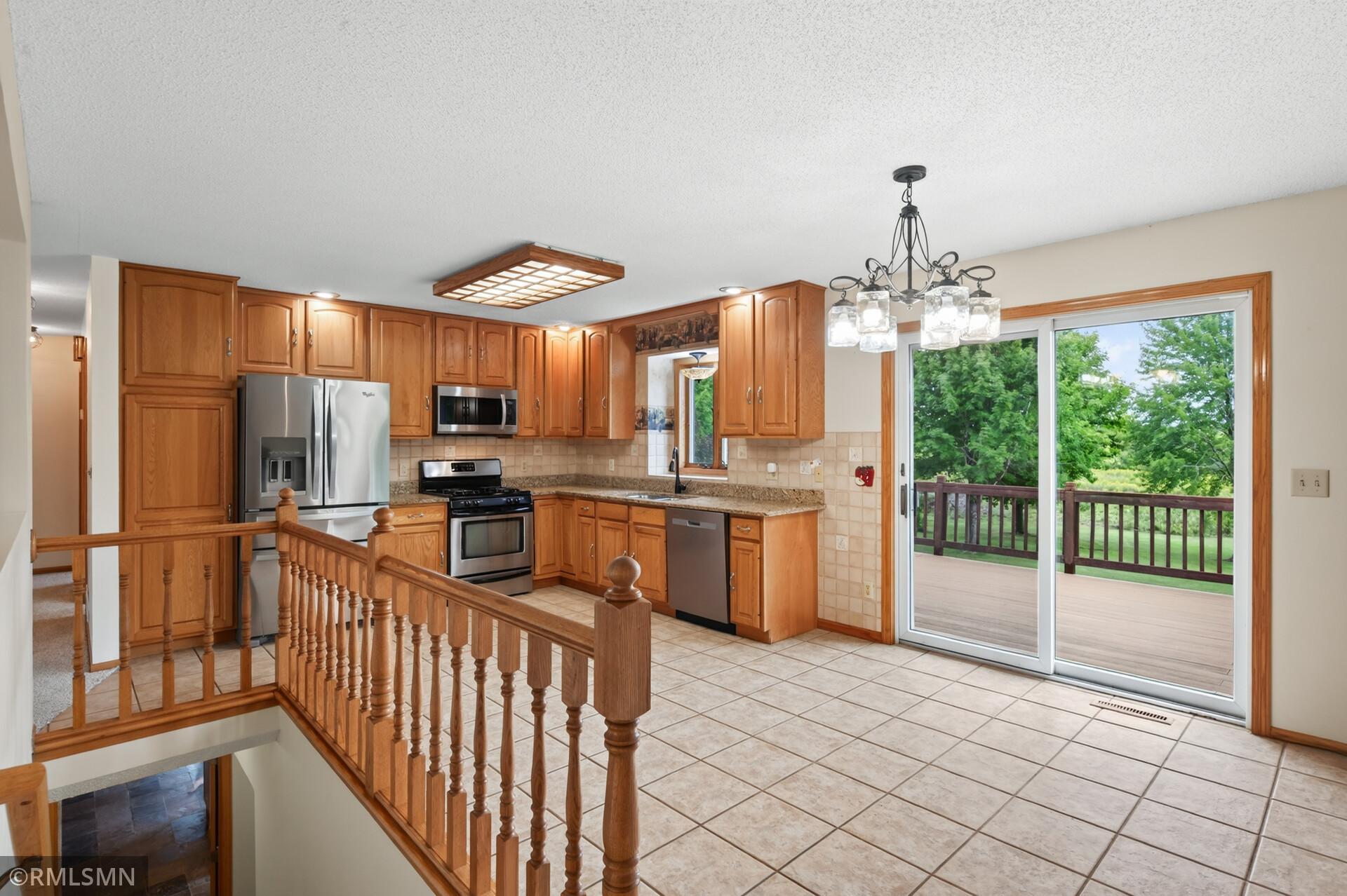Kitchen with warm wood cabinetry, stainless steel appliances, tiled floors, and sliding doors to a deck.