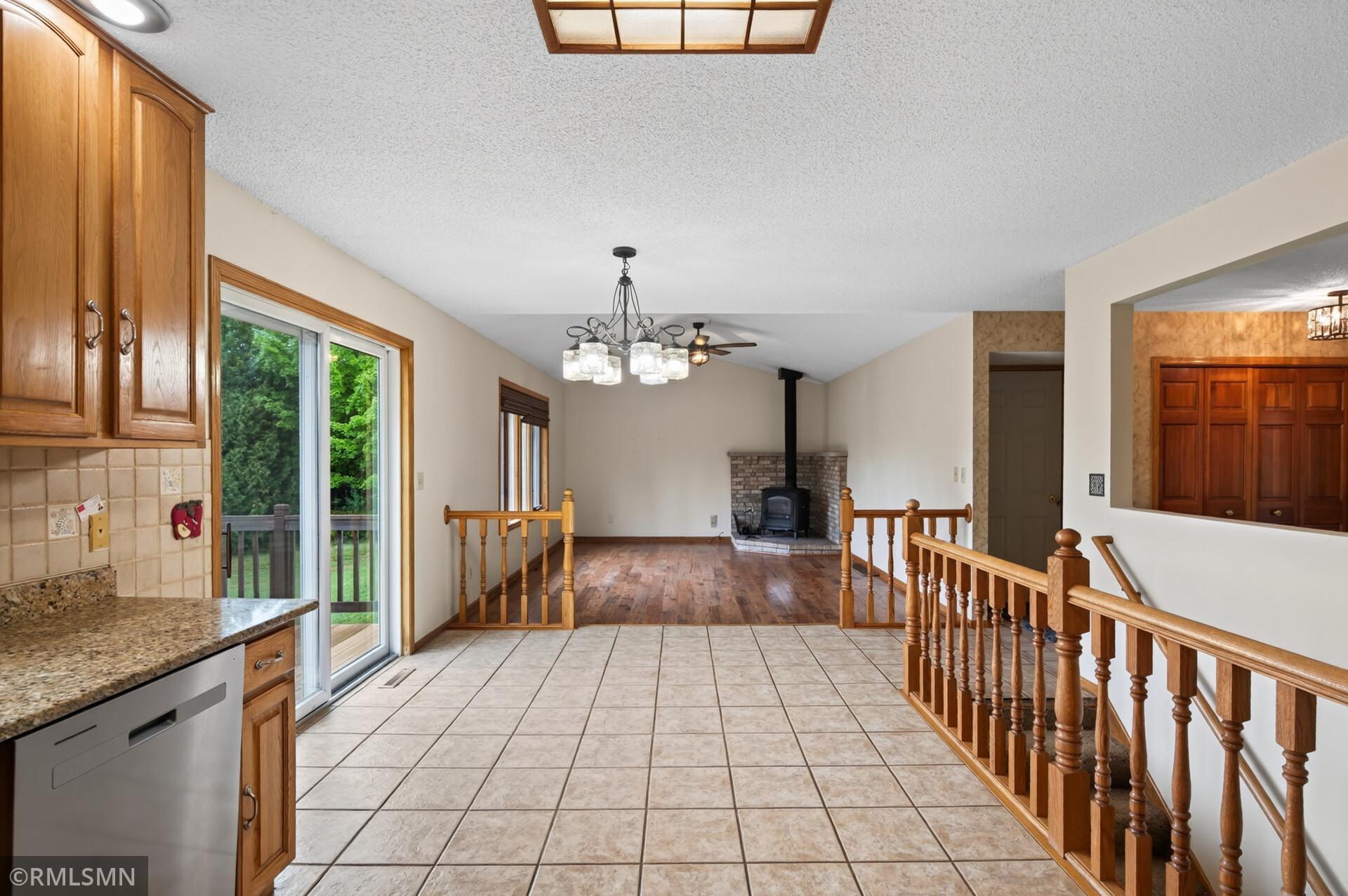 Open kitchen and living area with wood cabinets, tiled floor, and a brick fireplace with a black stove.