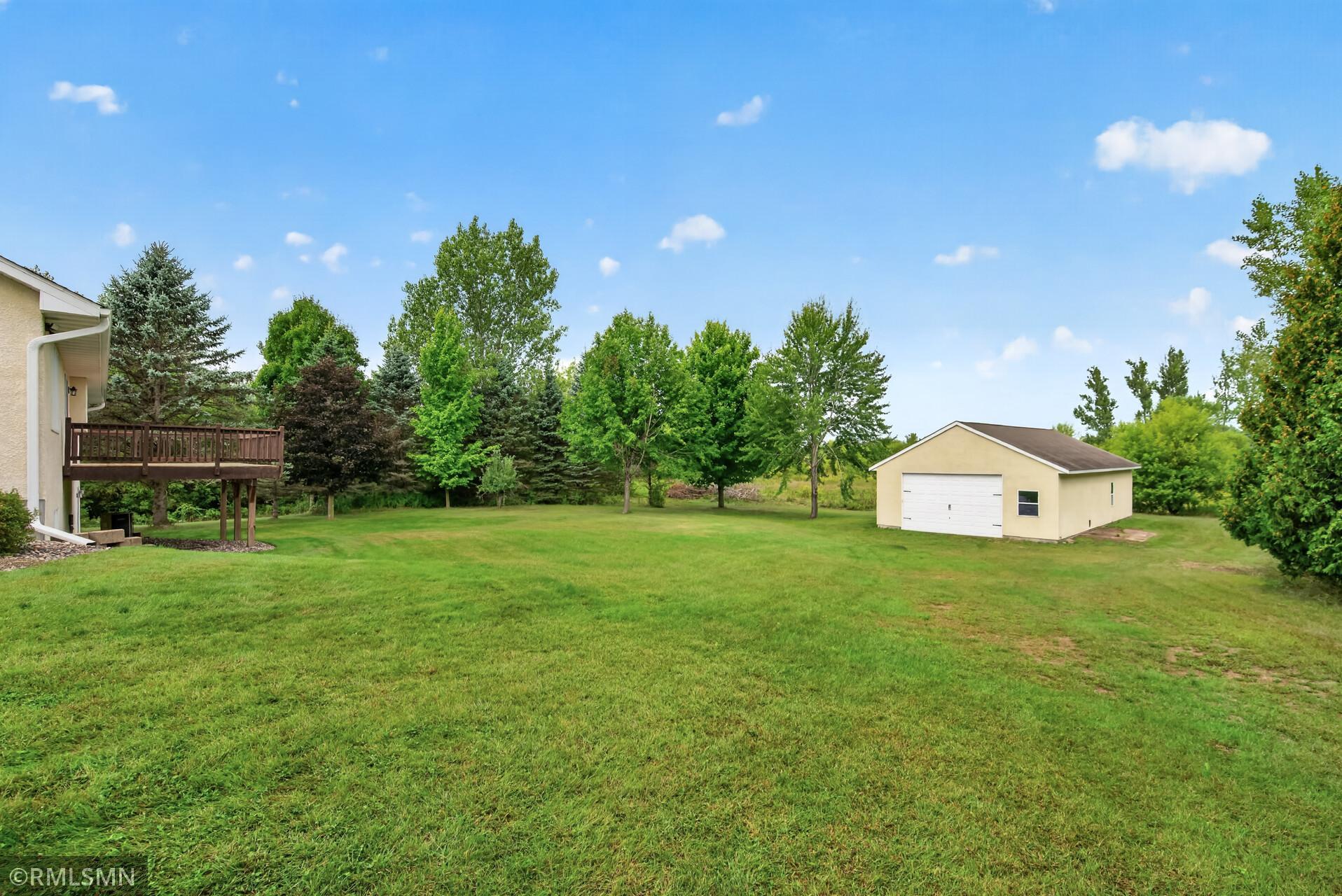 Spacious grassy backyard with a detached garage, mature trees, and a raised deck beside the house.