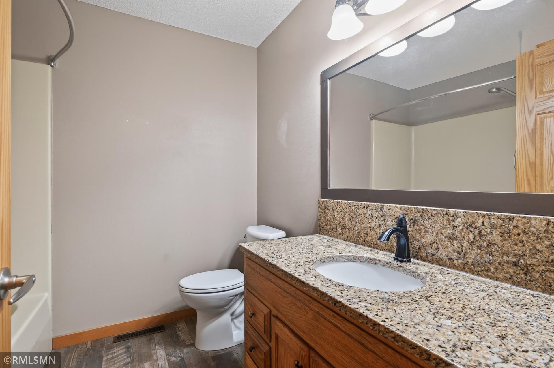 Bathroom with granite vanity, wood cabinetry, and tub-shower.