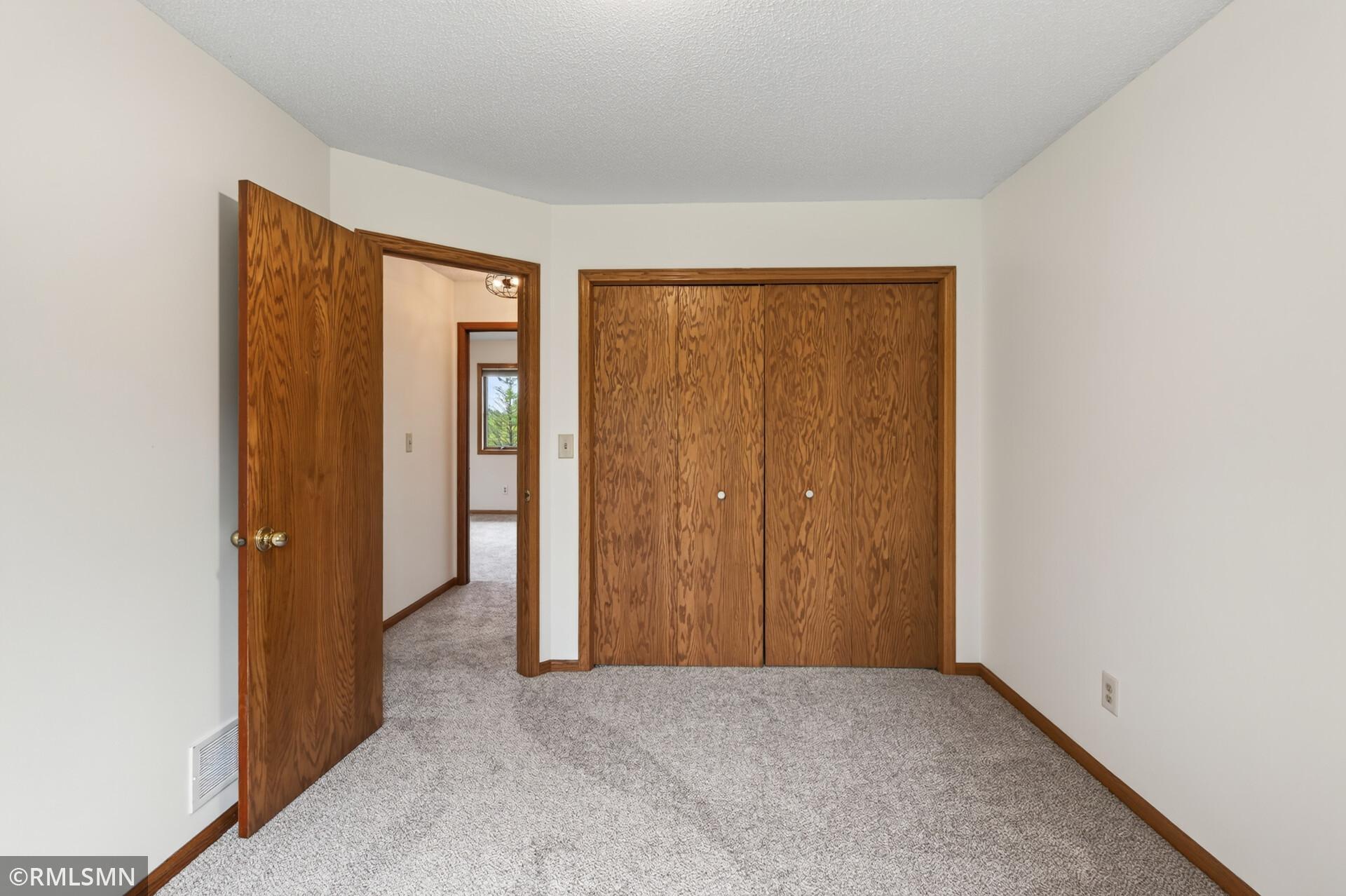 Empty bedroom with gray carpet, wood sliding closet doors, and an open doorway to the hall.