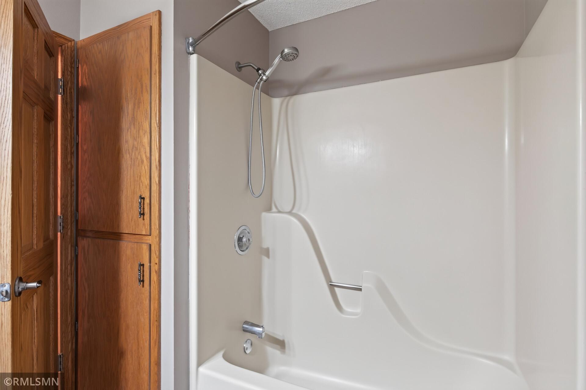 Bathroom tub-shower with a handheld showerhead beside warm wood cabinetry.