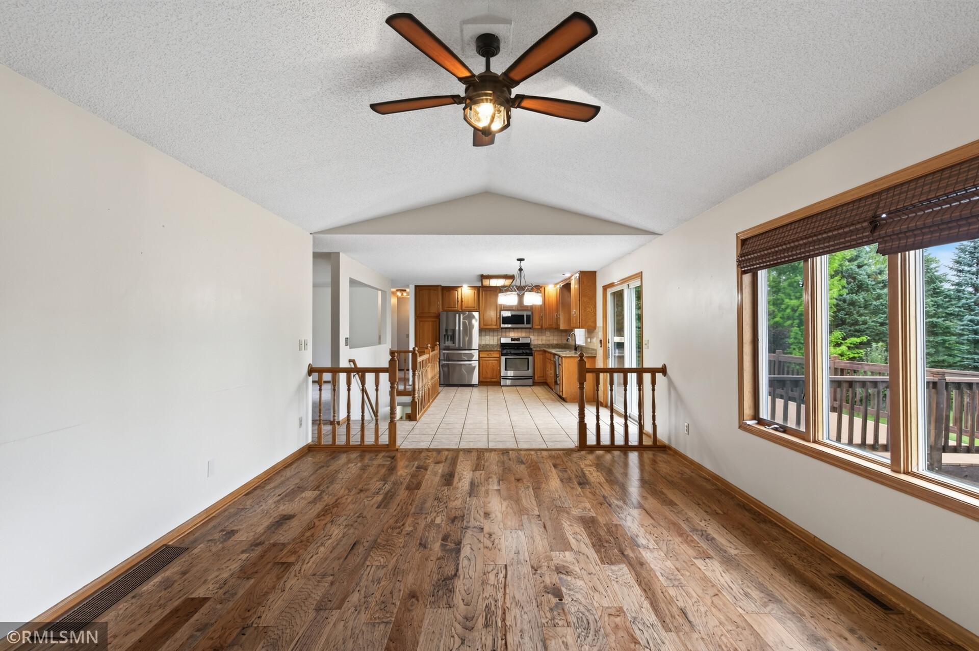 Open living area with vaulted ceiling and hardwood floors leading to a wood-cabinet kitchen.