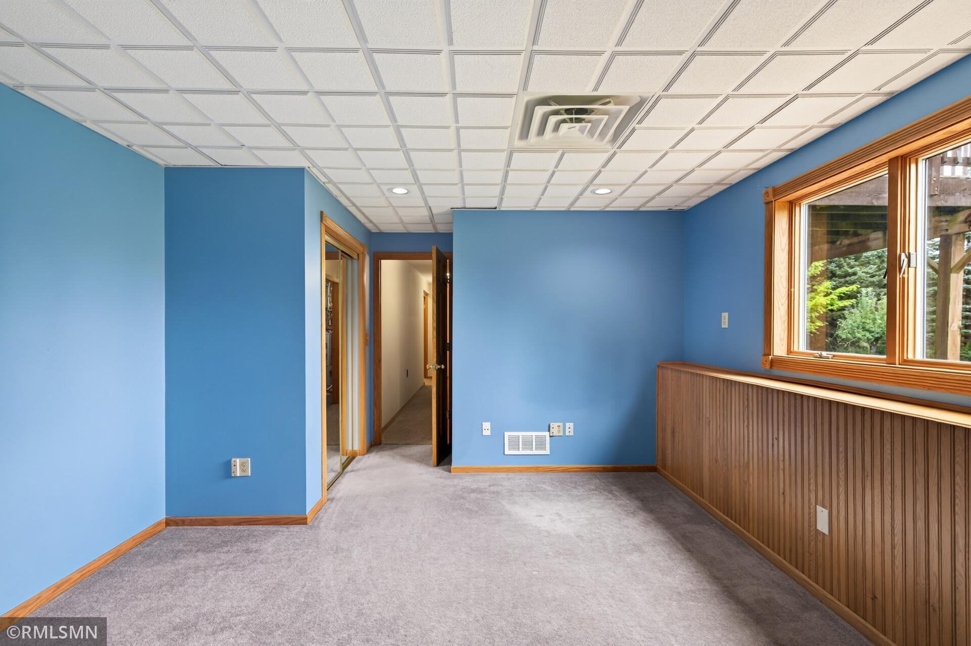 Empty blue room with gray carpet, wood-paneled walls, and a large window.