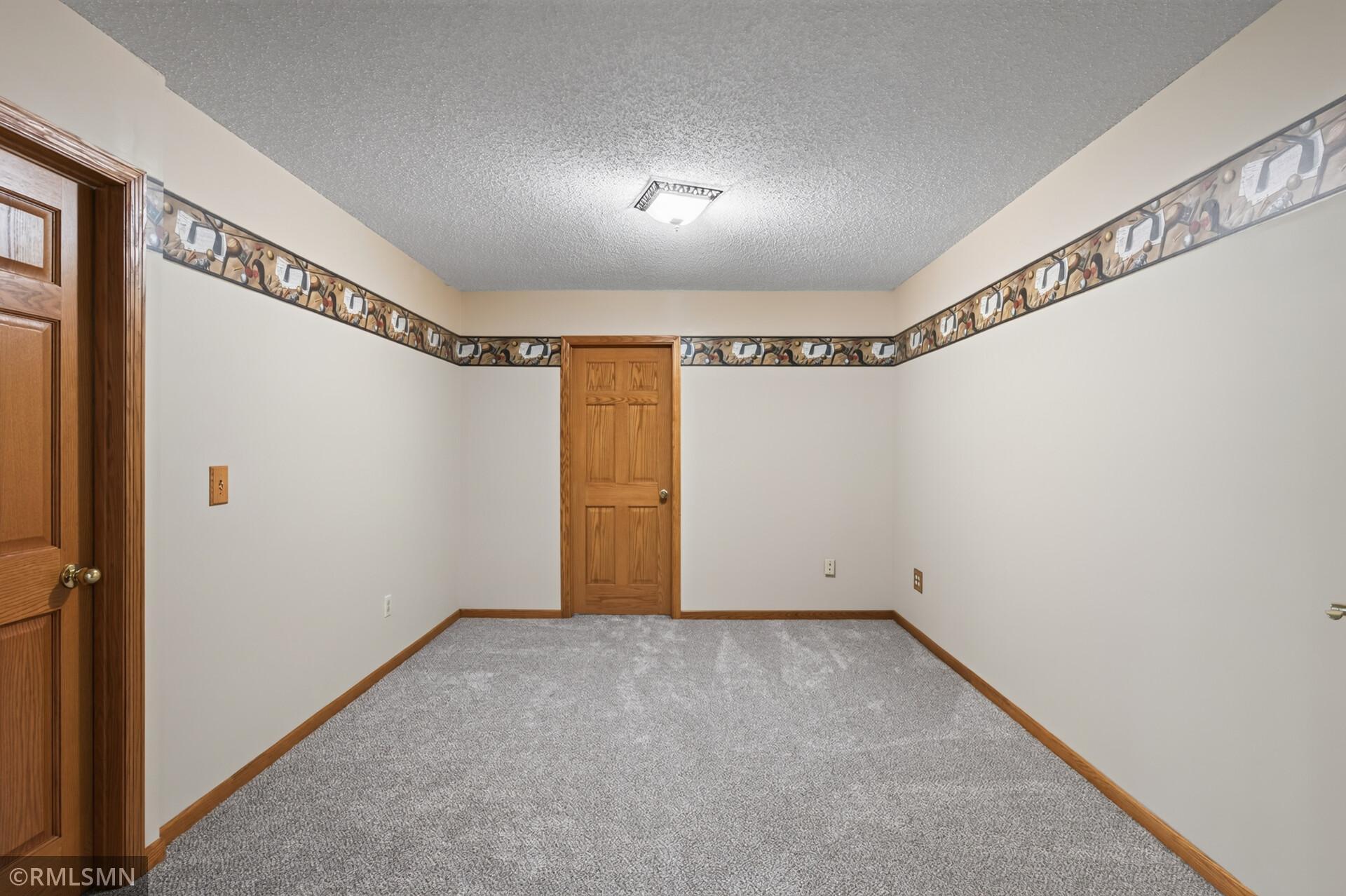 Empty carpeted room with wood trim, two wooden doors, and a decorative wall border.