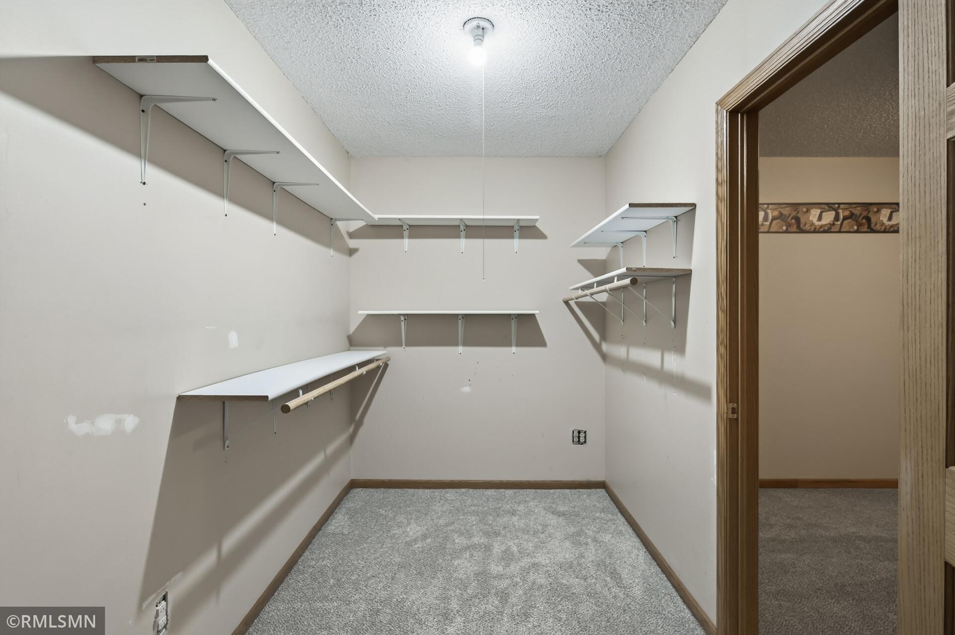 Walk-in closet with wall-mounted shelves and hanging rods, viewed through an open doorway.