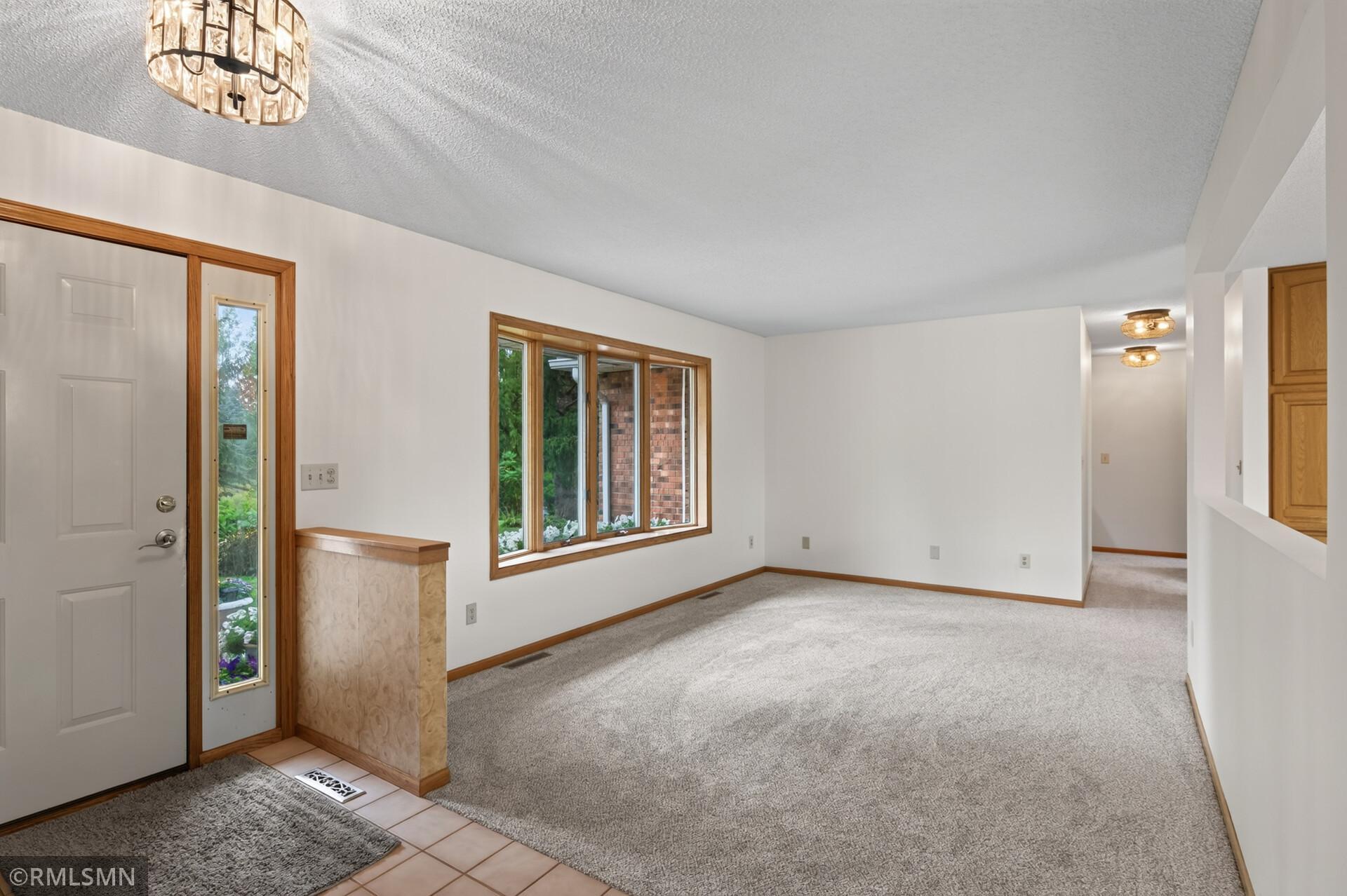 Empty carpeted entry area with a front door, sidelights, and large wood-trimmed window.