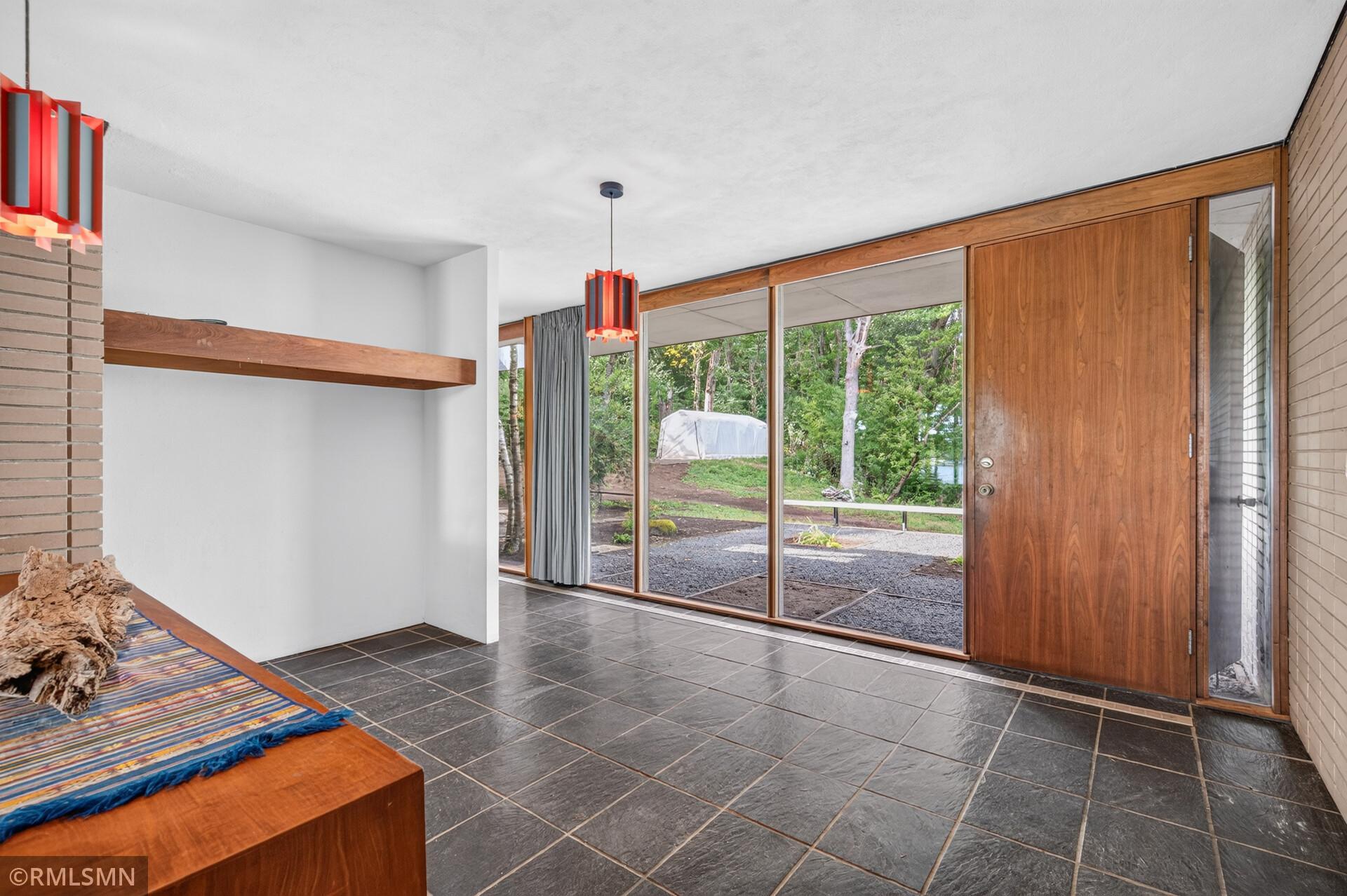 Mid-century modern entry with a large wood door, floor-to-ceiling windows, and a built-in bench.