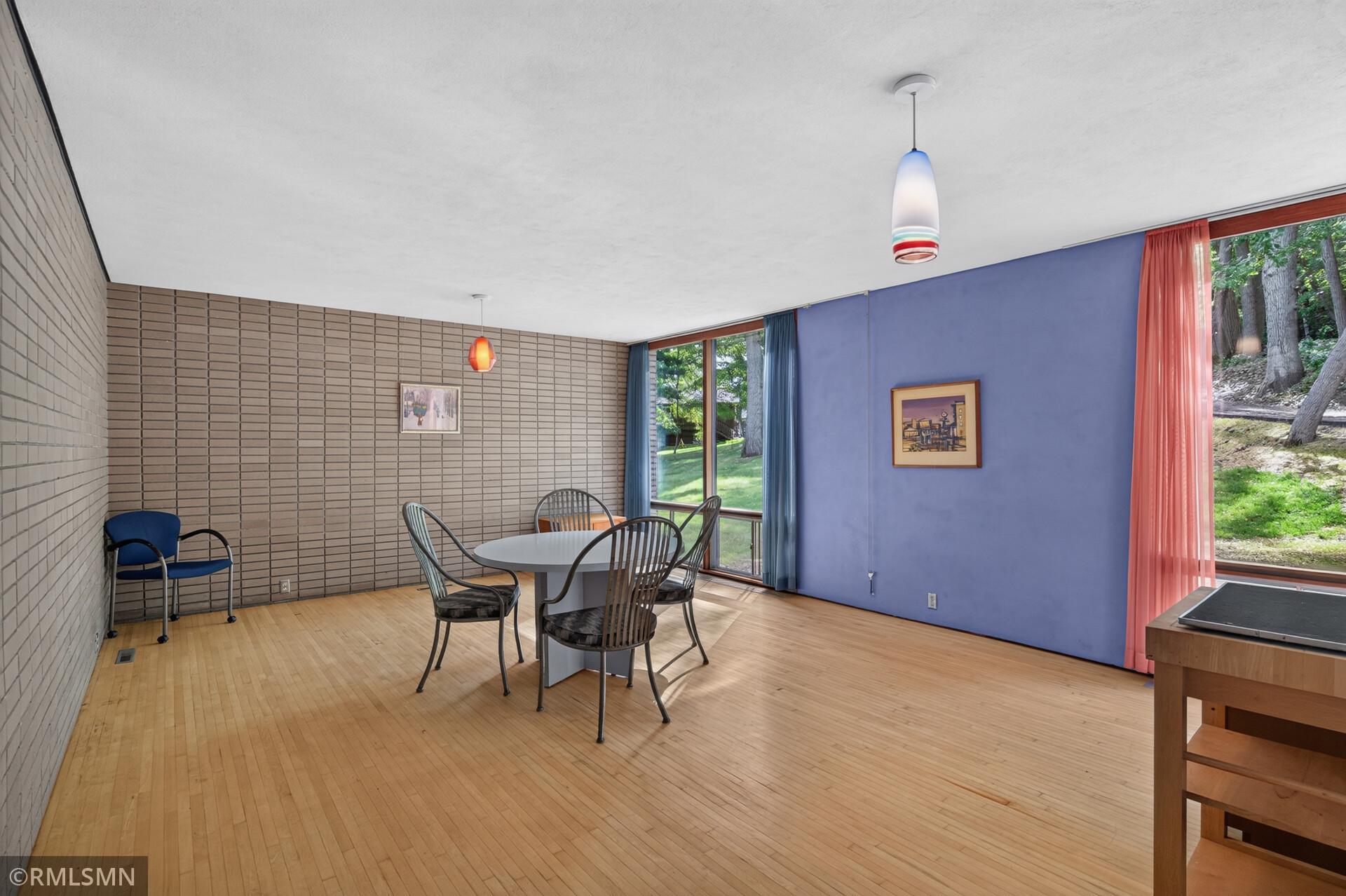 Dining room with hardwood floors, colorful pendant lights, and large windows overlooking a wooded yard.