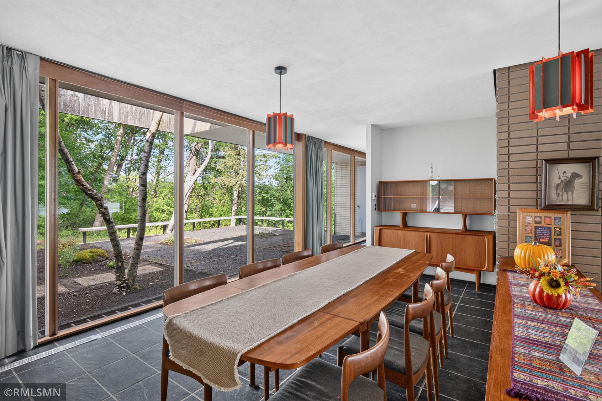 Dining room with a long wooden table and expansive windows overlooking trees and a patio.