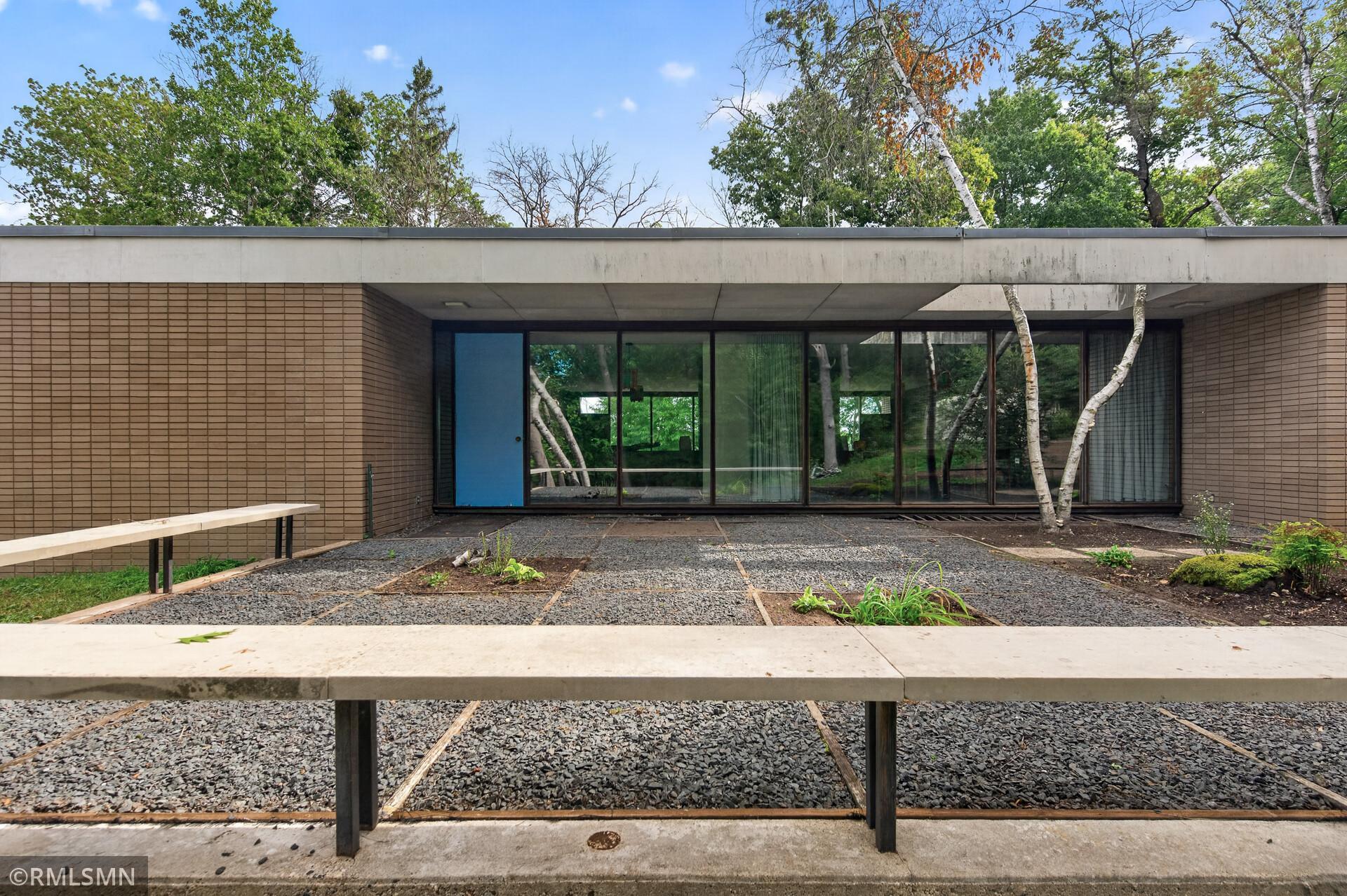 Modern brick home with a flat roof, blue door, and broad windows facing a gravel courtyard.