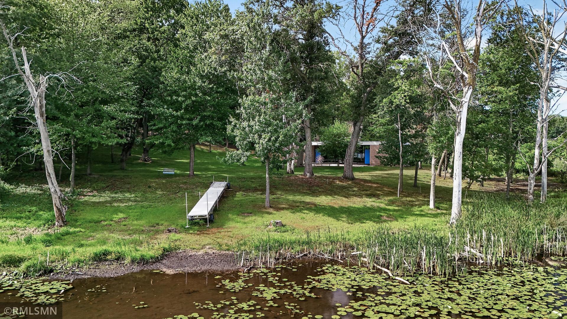 Wooded waterfront yard with a dock, lily pads, and a brick house among the trees.
