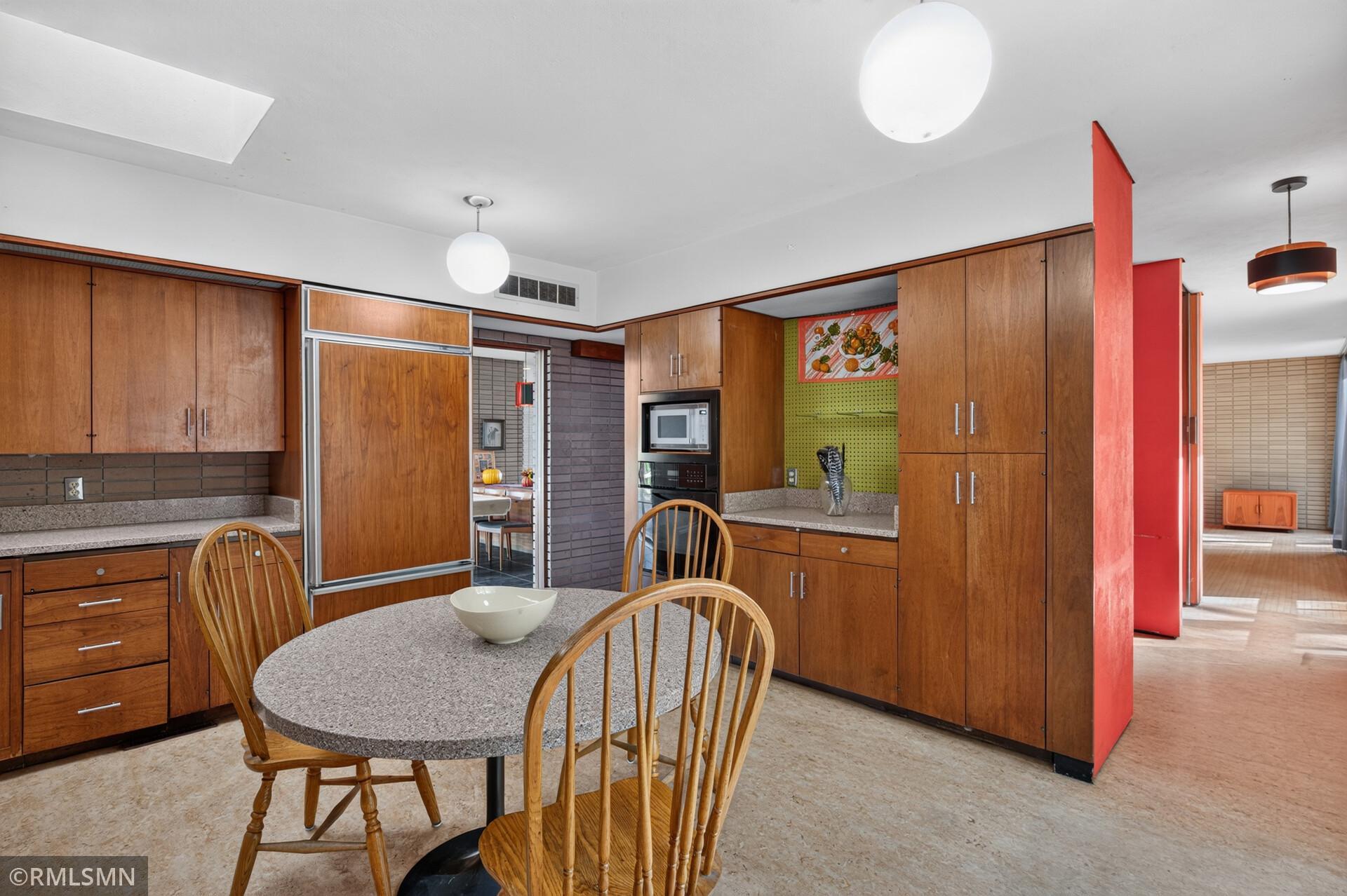 Mid-century kitchen with warm wood cabinets, a rounded dining table, and bold red divider panels.