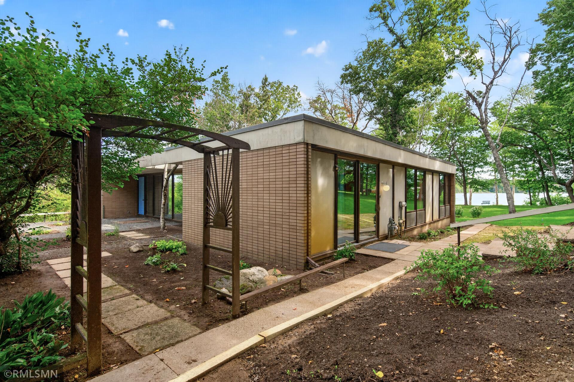 Modern brick home with a wooden pergola and lake visible through the trees.
