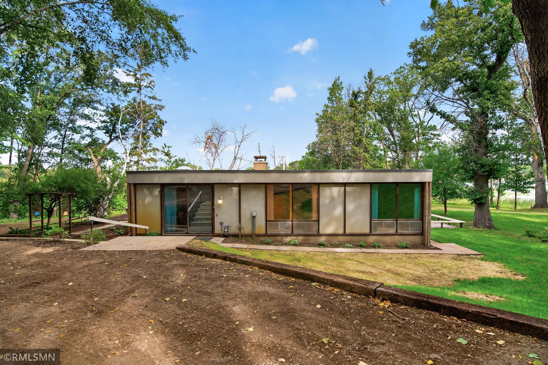 Modern flat-roofed home with broad windows in a leafy, tree-shaded yard.