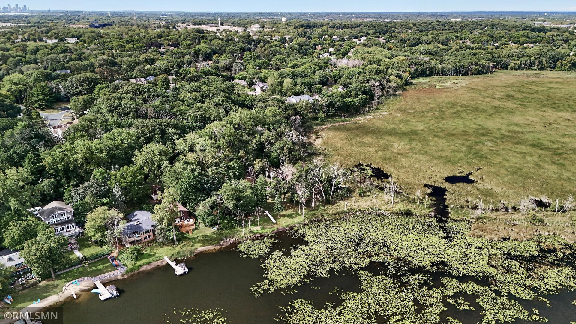 Aerial view of lakeside homes and docks beside a lily-pad-covered lake and marsh.