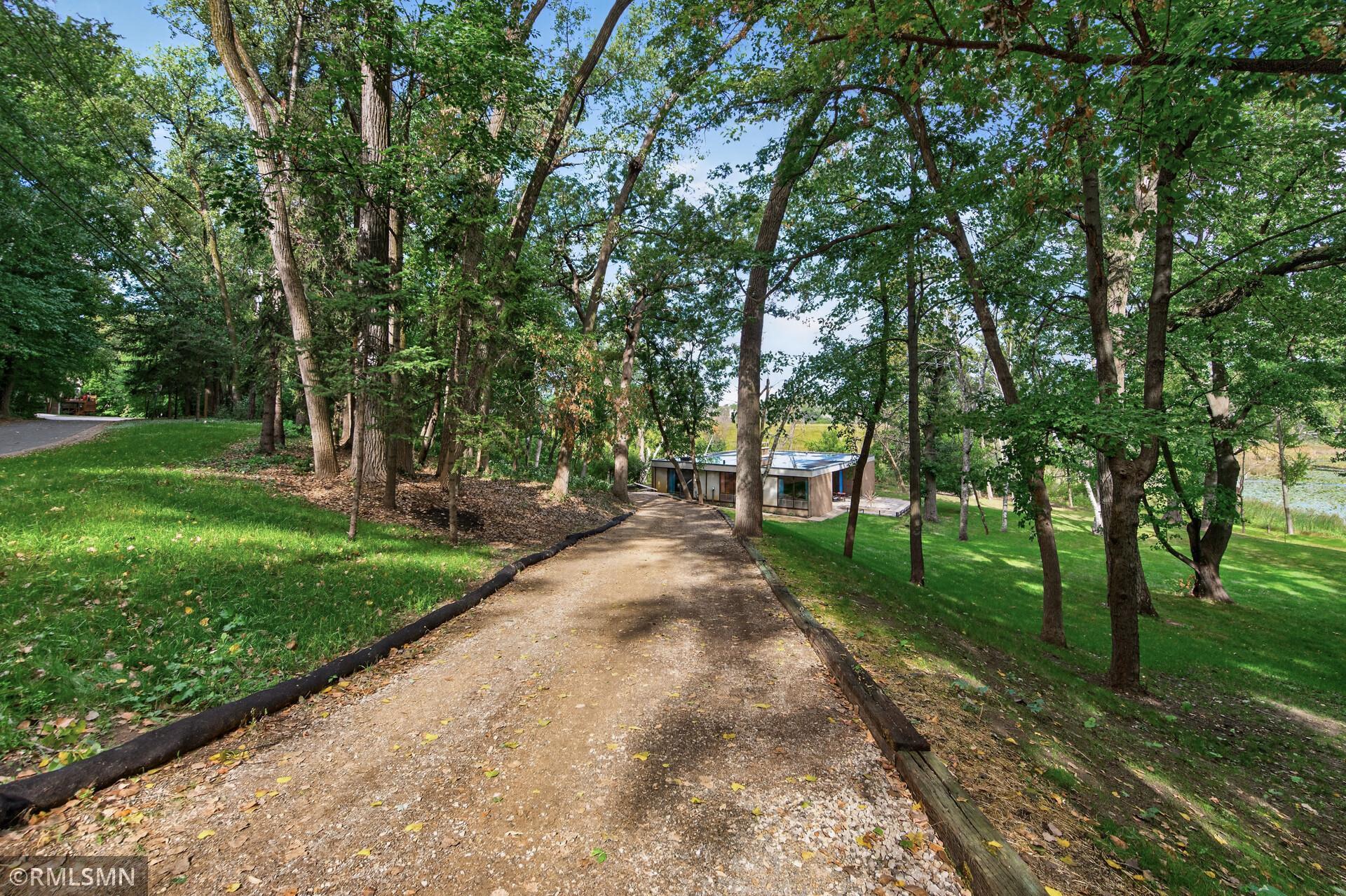Wooded property with a winding gravel driveway leading to a modern home beside a small pond.