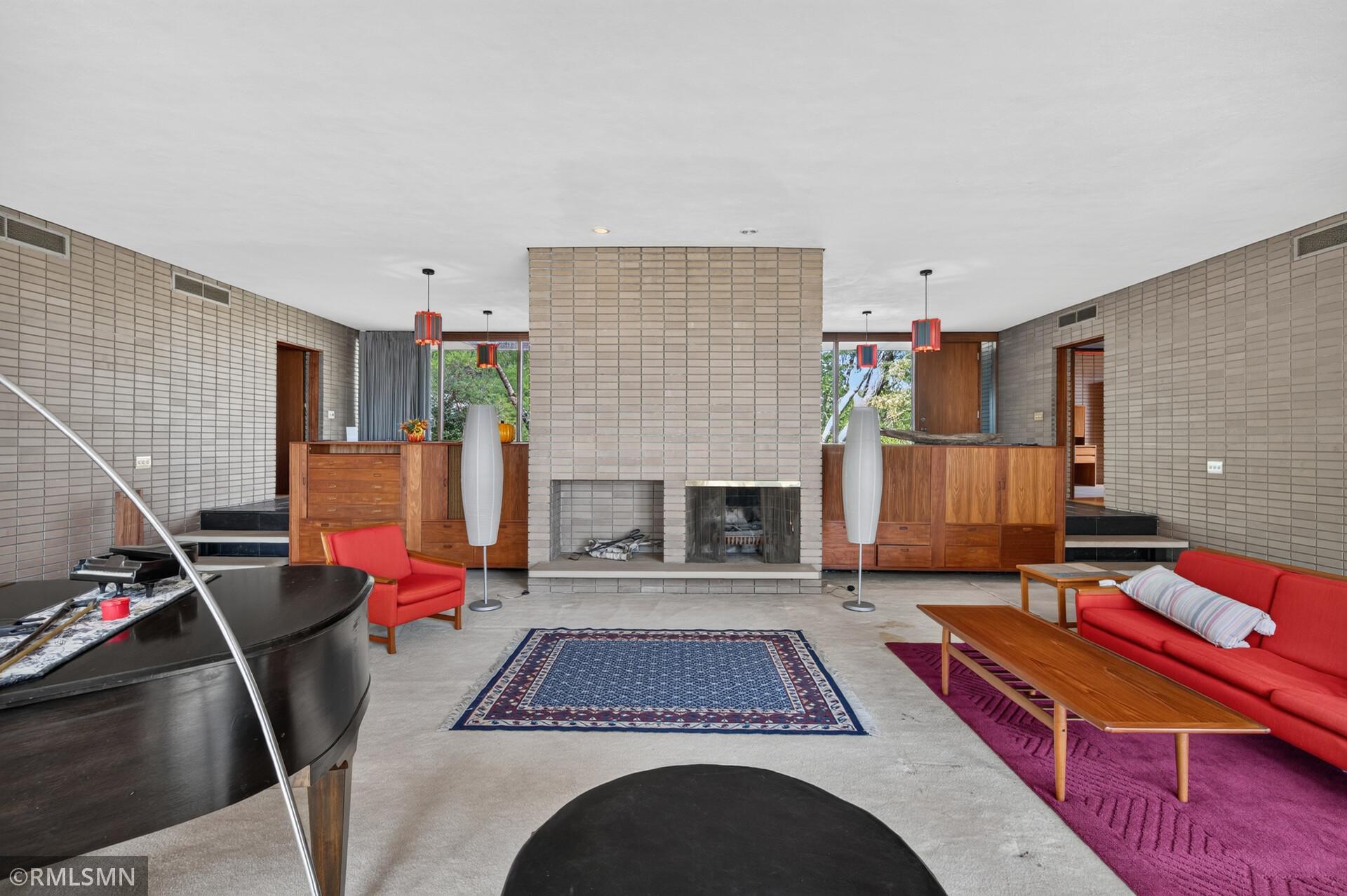Living room with a central brick fireplace, mid-century wood cabinetry, and red seating.