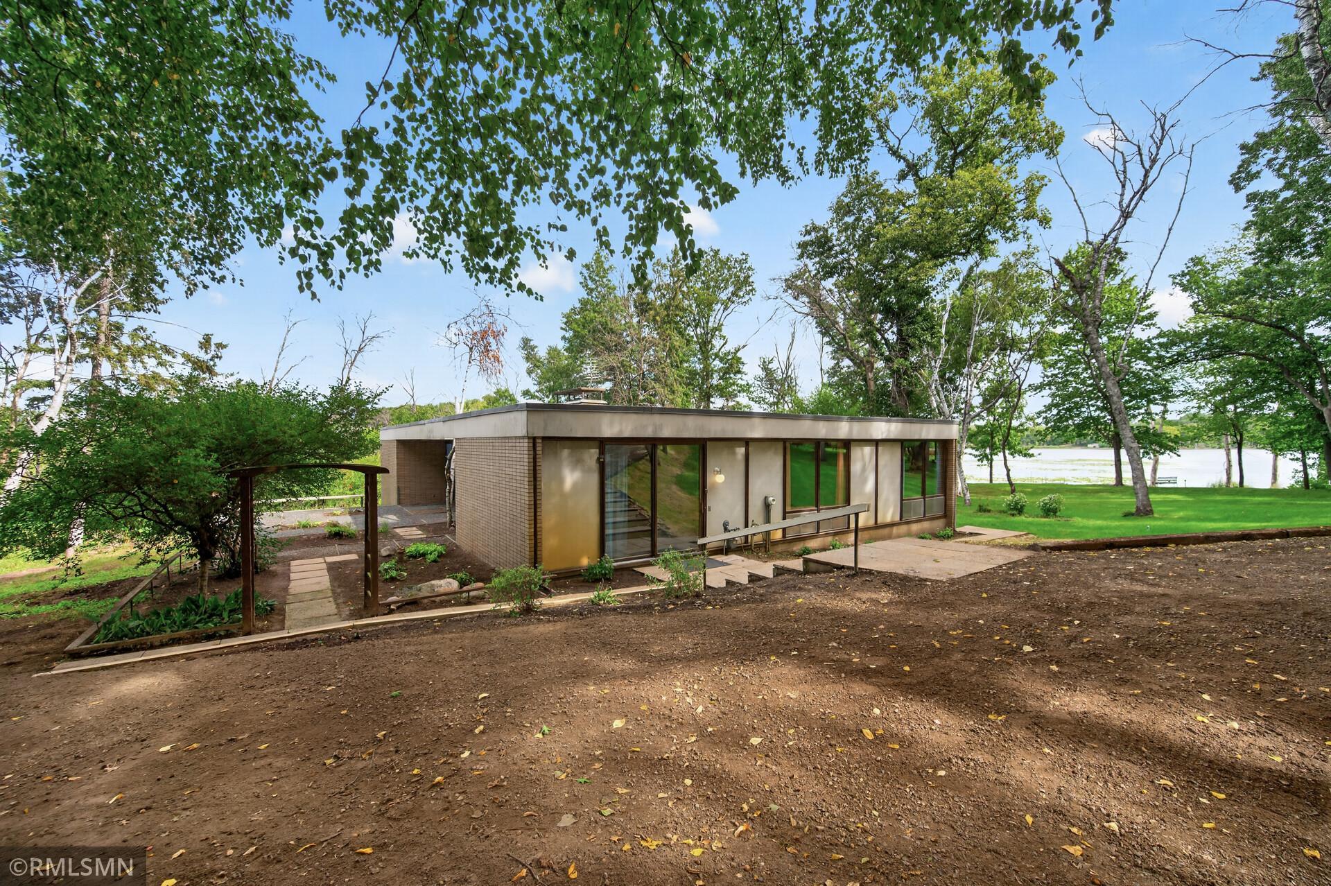 Flat-roofed mid-century modern home with expansive windows, a patio, and a lake view.