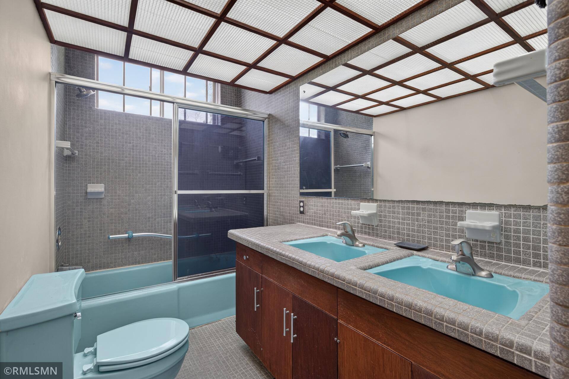 Bathroom with turquoise tub and shower, double-sink vanity, gray tile, and a grid ceiling with wood beams.