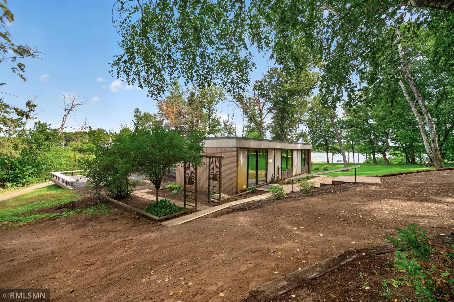 Low-profile brick home with broad windows, garden beds, and lake visible through mature trees.