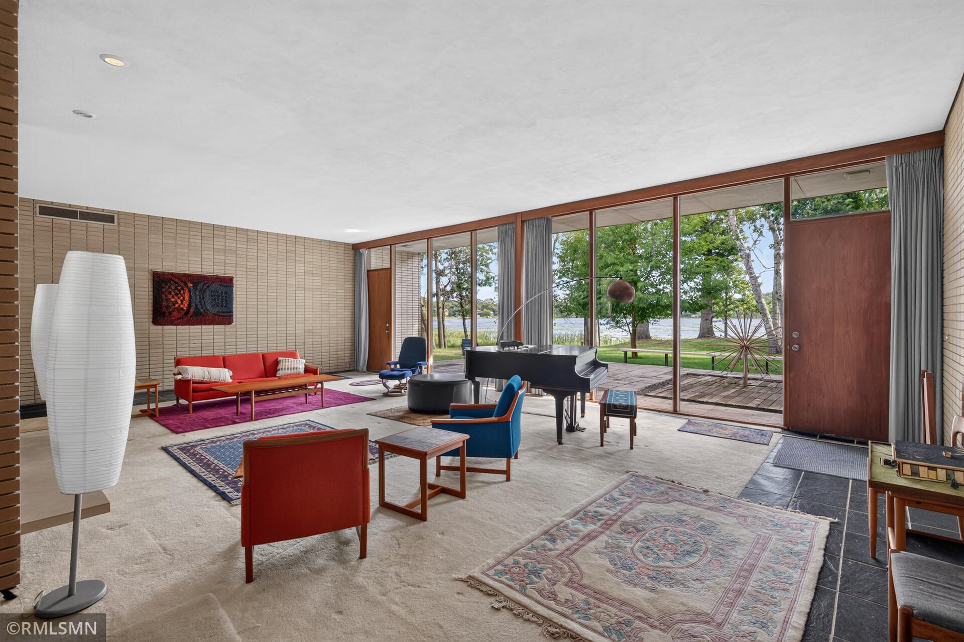 Mid-century living room with a grand piano and floor-to-ceiling windows overlooking a lake.