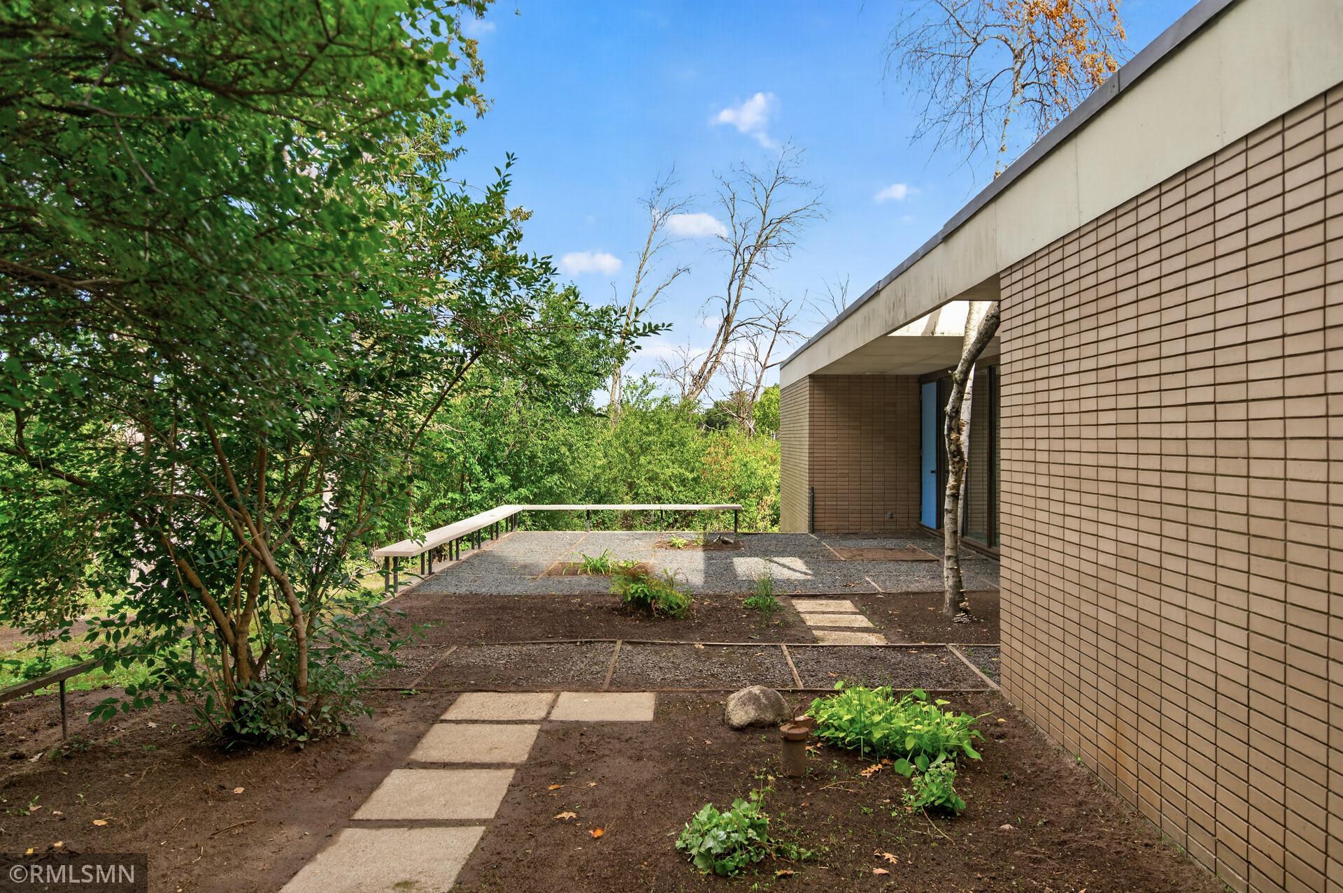 Modern brick-sided home beside a gravel patio and leafy garden.