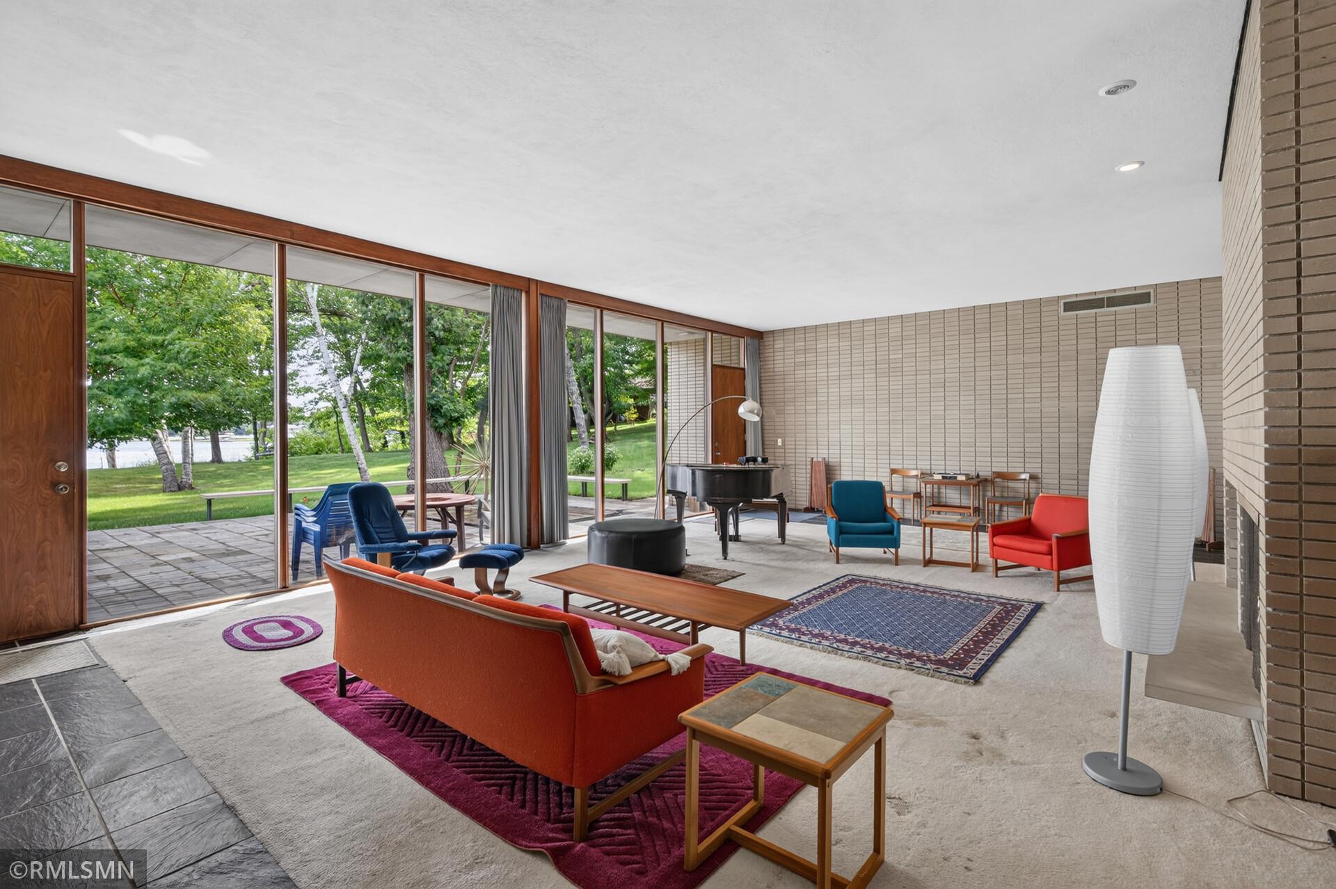 Furnished living room with floor-to-ceiling windows overlooking a lake and green grounds.