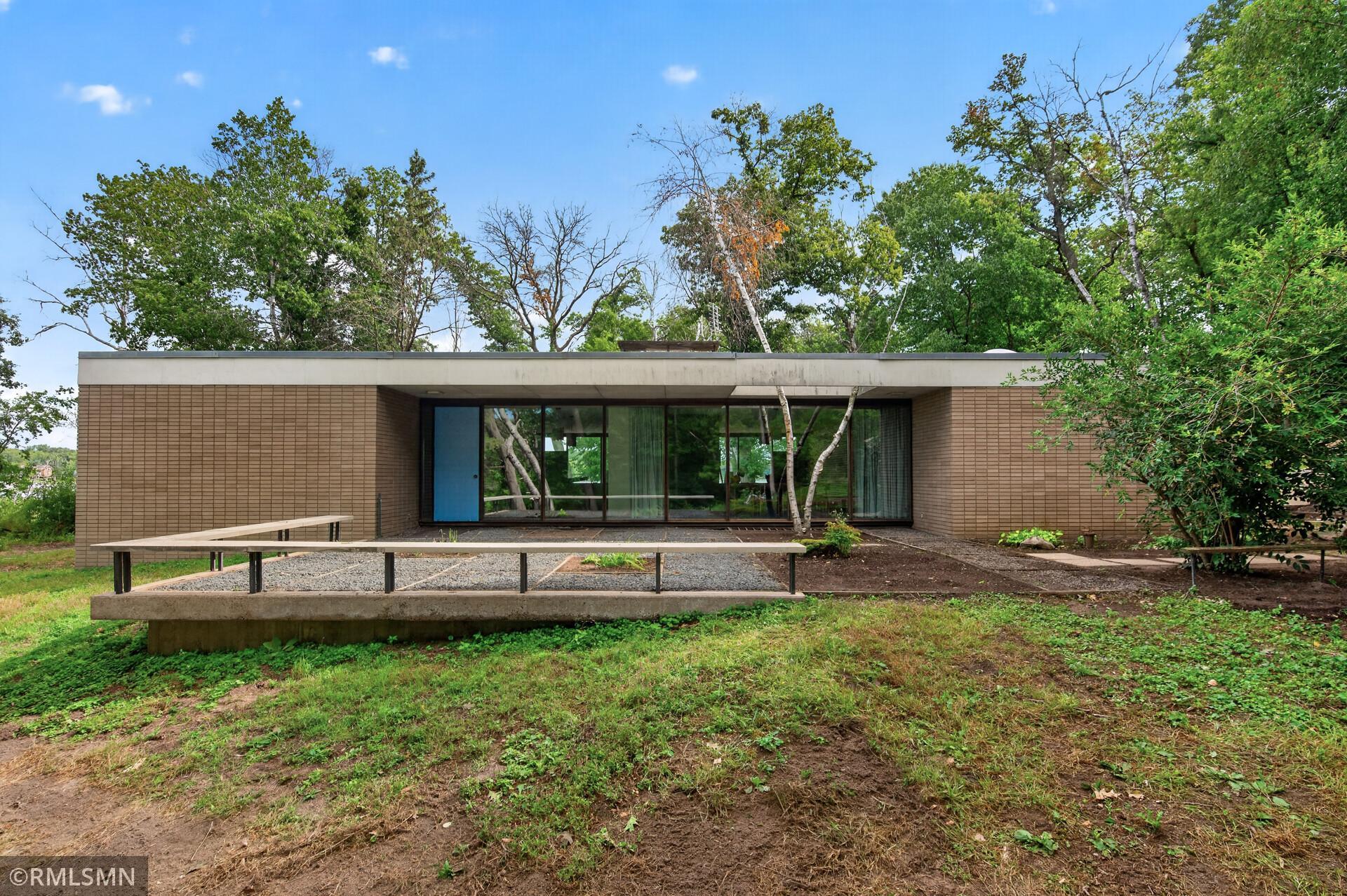 Modern brick home with a blue door, broad windows, and a raised concrete walkway.