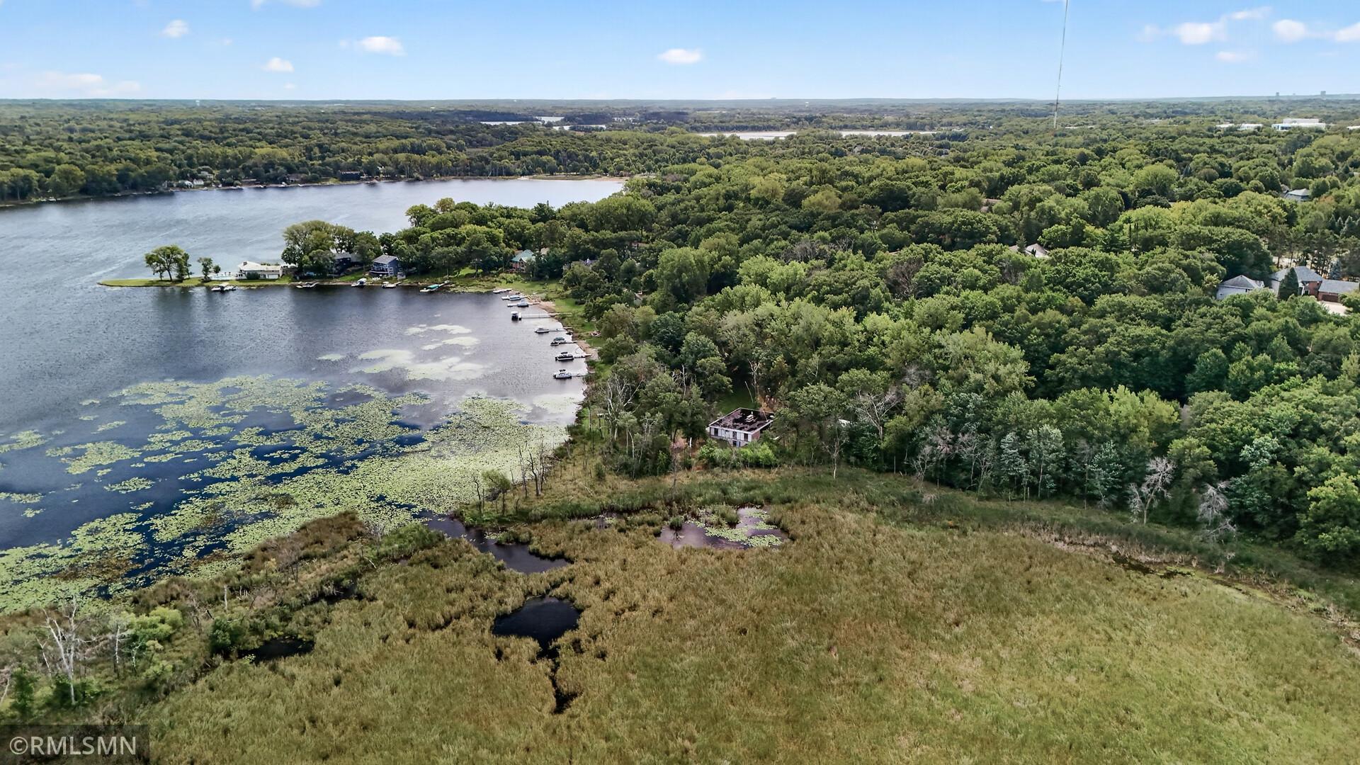 Aerial view of a wooded lakeshore, docks, and marshland beside open water.