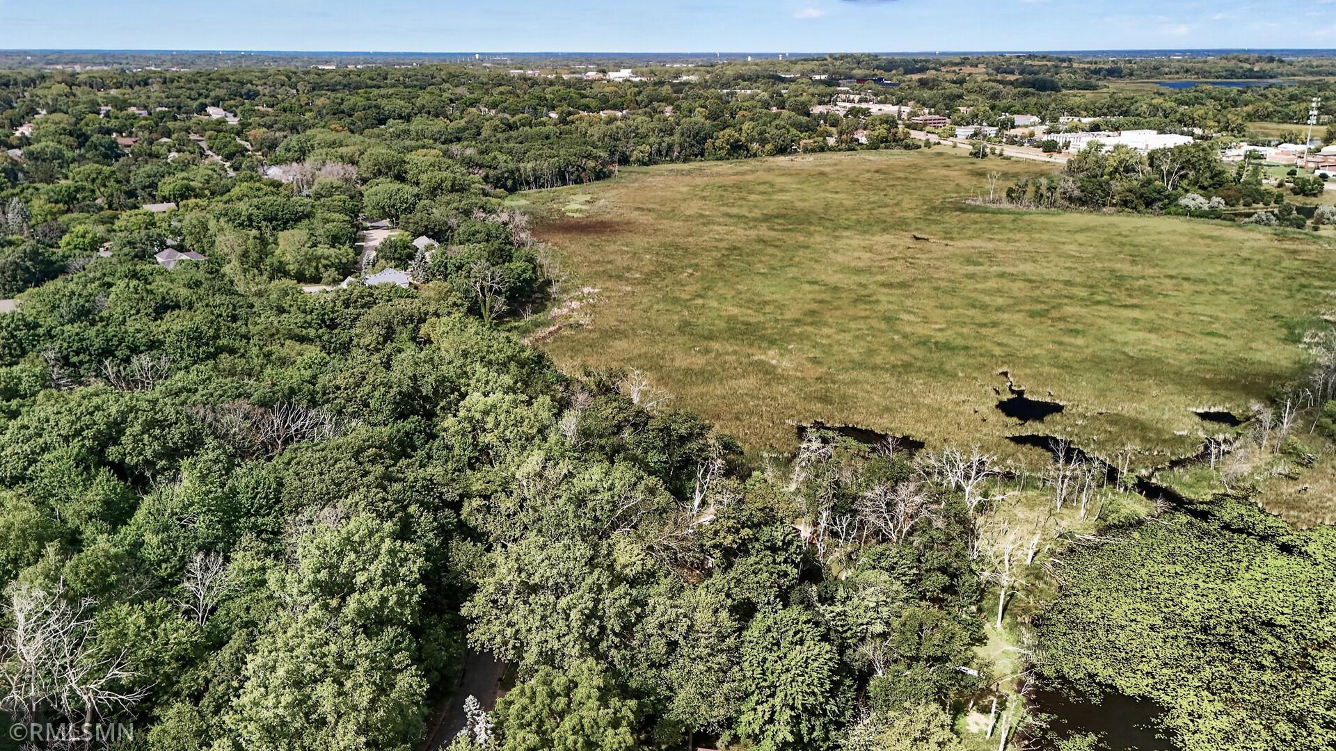 Aerial view of an open grassy wetland bordered by trees, with ponds and nearby homes.