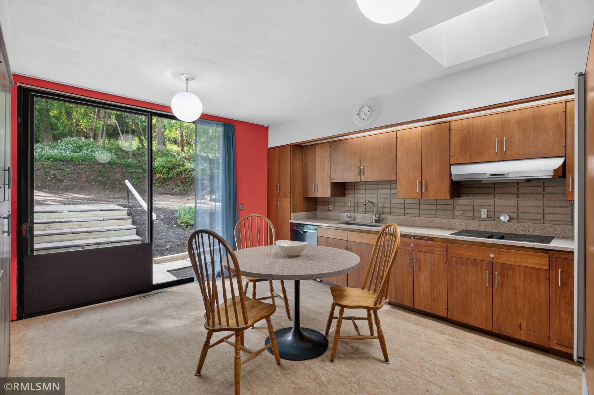 Kitchen with wood cabinetry and dining table beside a sliding glass door overlooking wooded steps.
