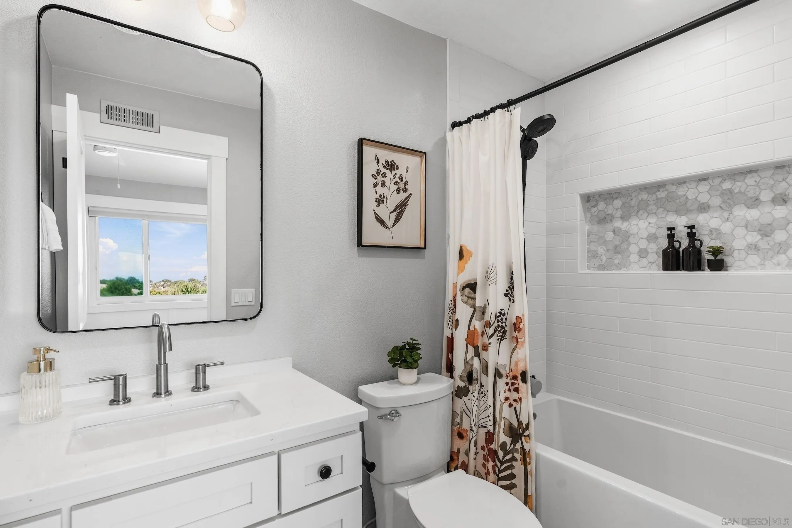 Bathroom with a white vanity and black-framed mirror beside a subway-tile tub with a mosaic niche.