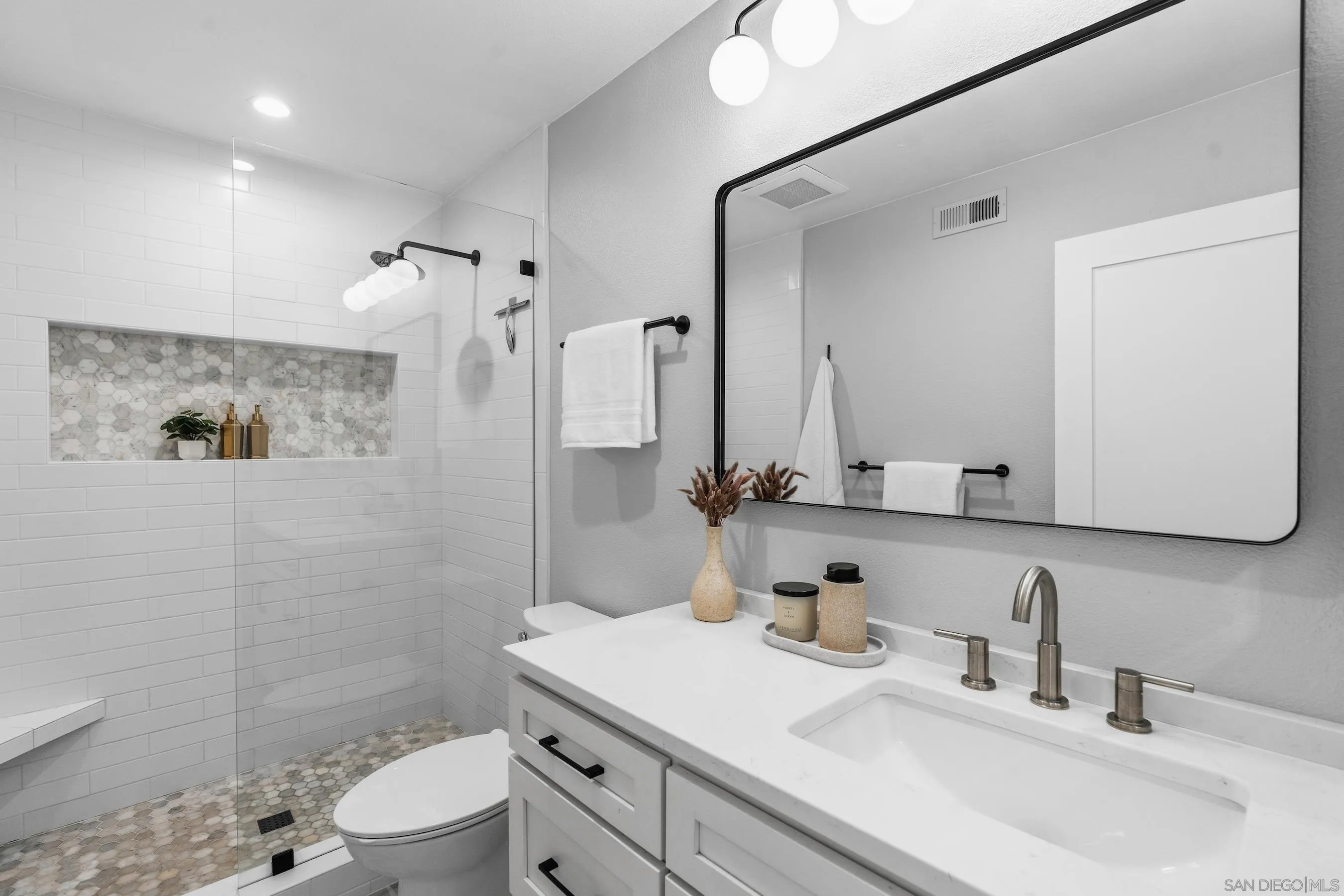 Renovated bathroom with a glass shower, mosaic tile accents, and a white vanity beneath a black-framed mirror.