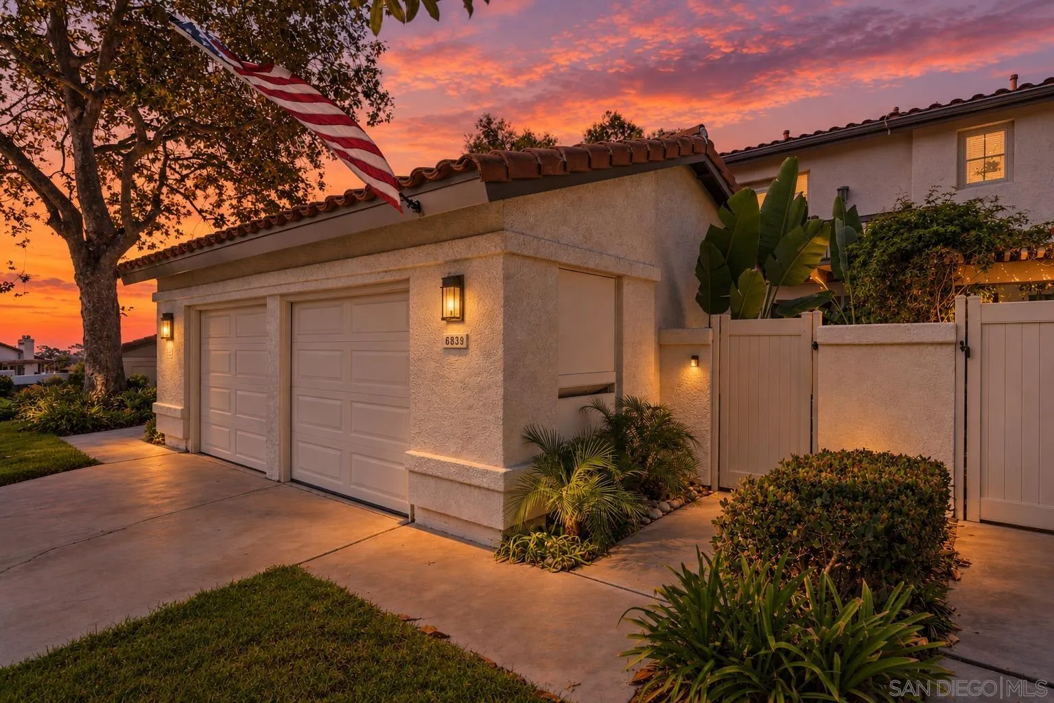 Stucco home exterior with double garage, American flag, and sunset sky.