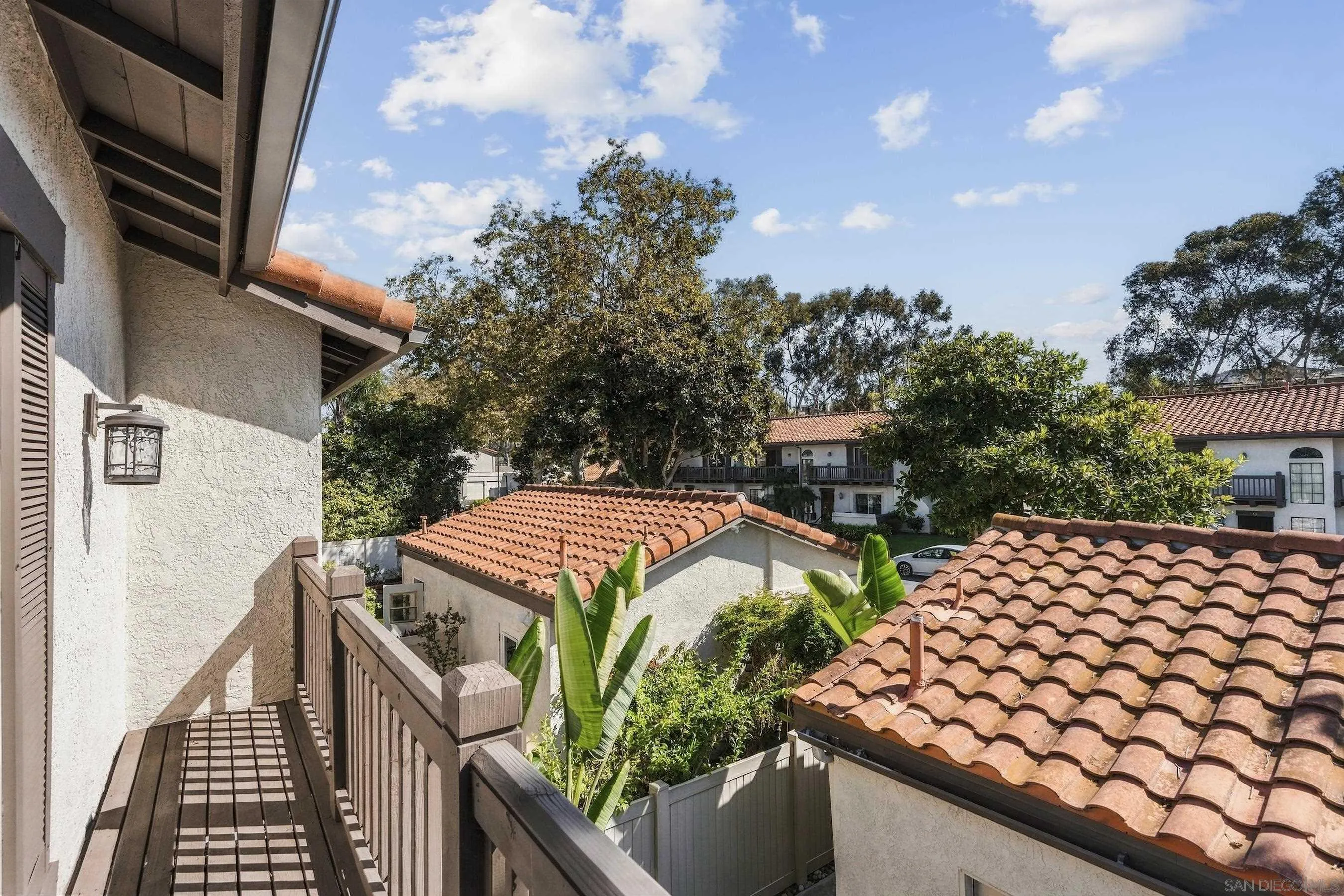 Balcony overlooking terracotta-tiled roofs, leafy trees, and neighboring stucco homes.