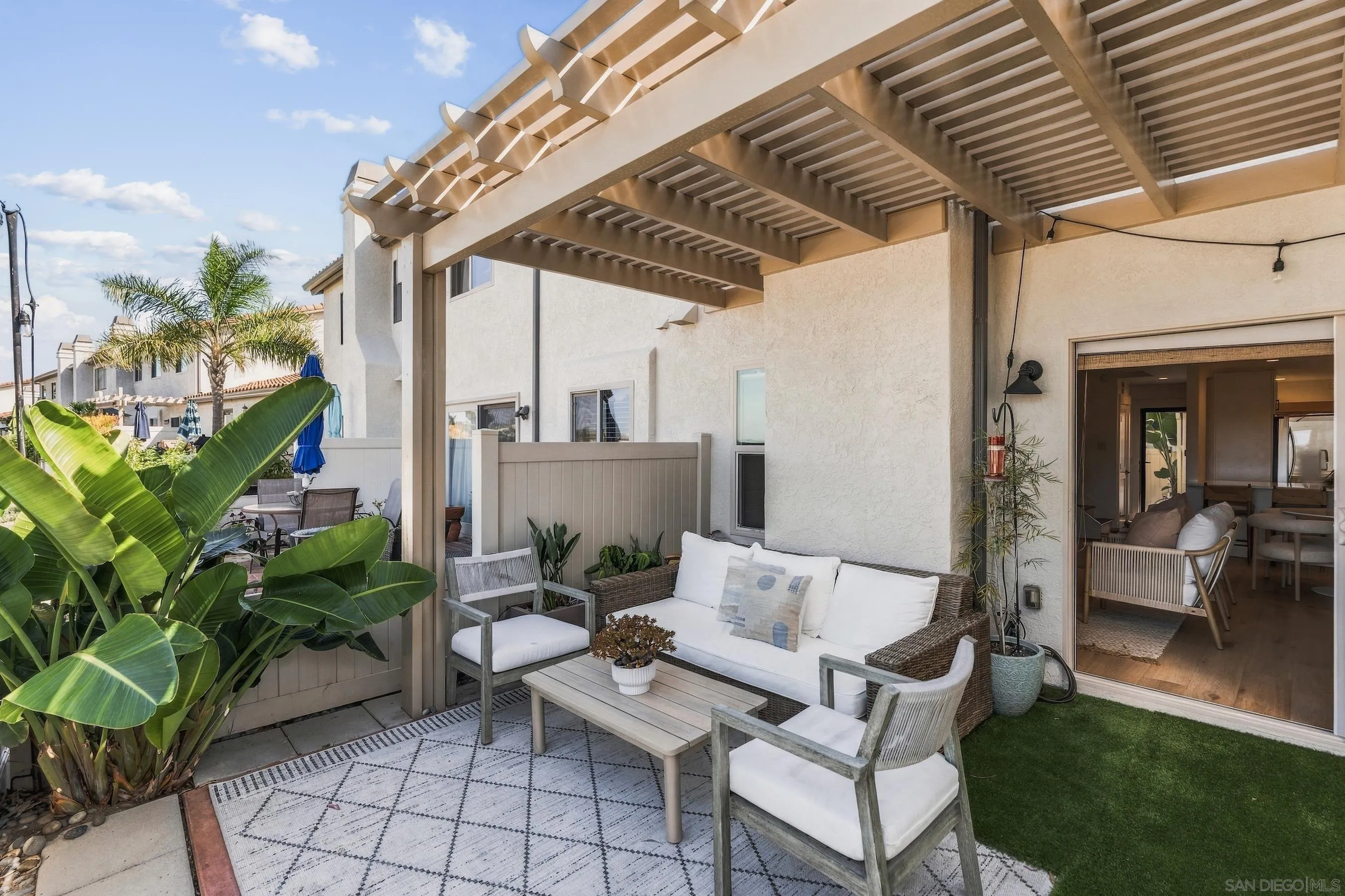 Covered patio with wicker seating, a pergola, tropical plants, and open doors to the home.