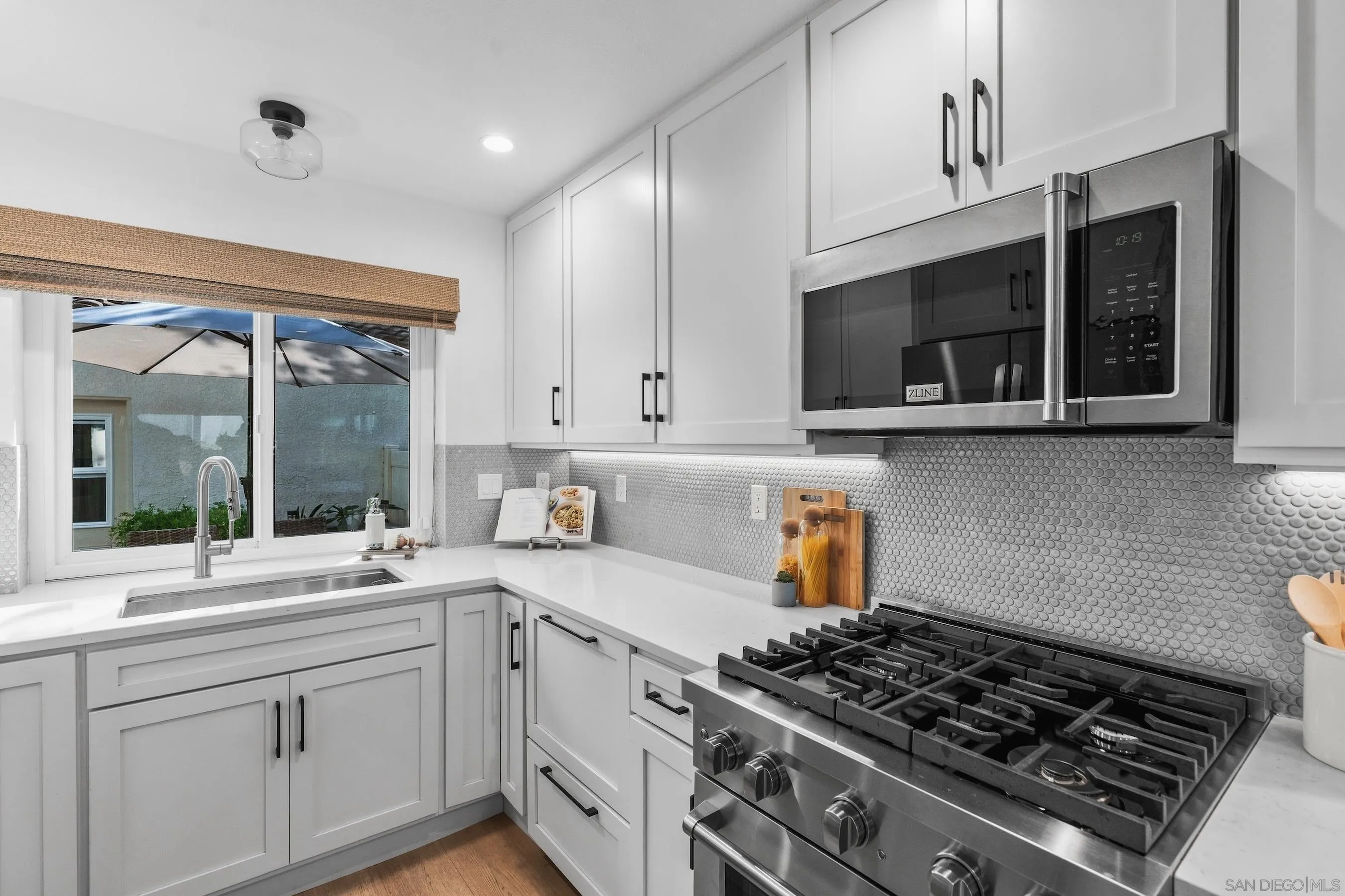 Renovated kitchen with white cabinets, stainless steel range, patterned backsplash, and a window above the sink.