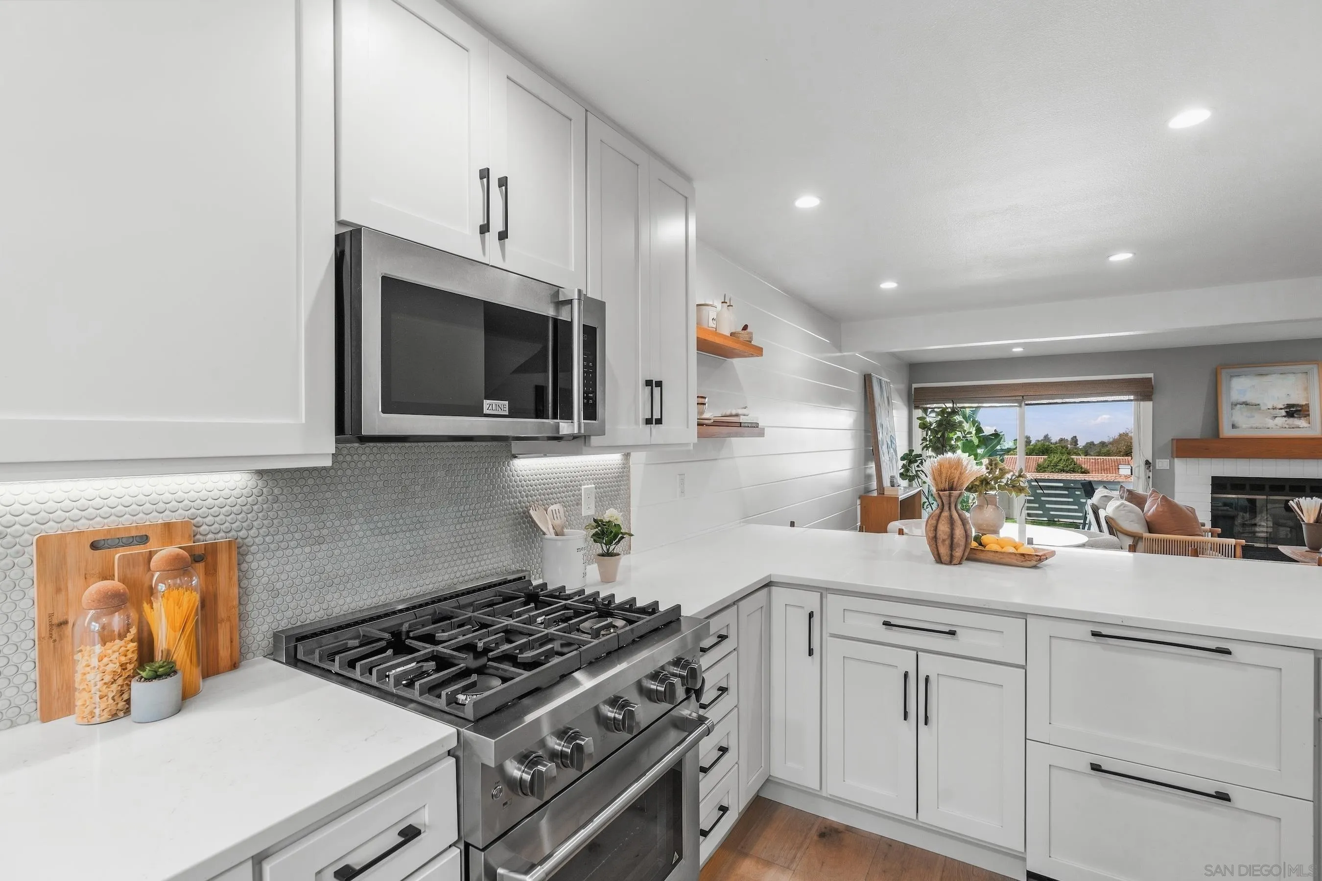 White kitchen with stainless-steel range, round-tile backsplash, and view into the living room and patio.