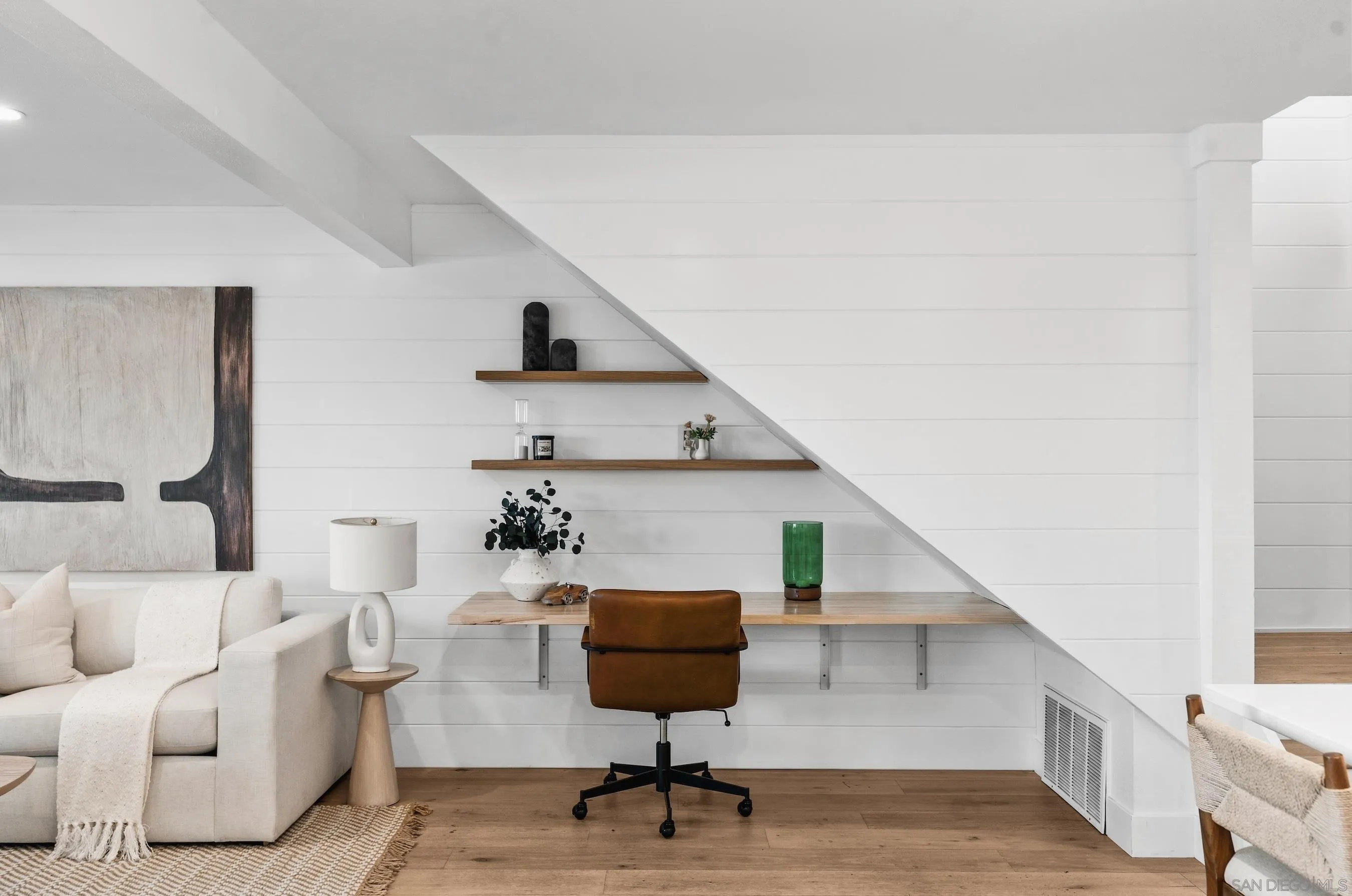 Living room with a desk beneath the staircase, floating shelves, and a cream sofa.