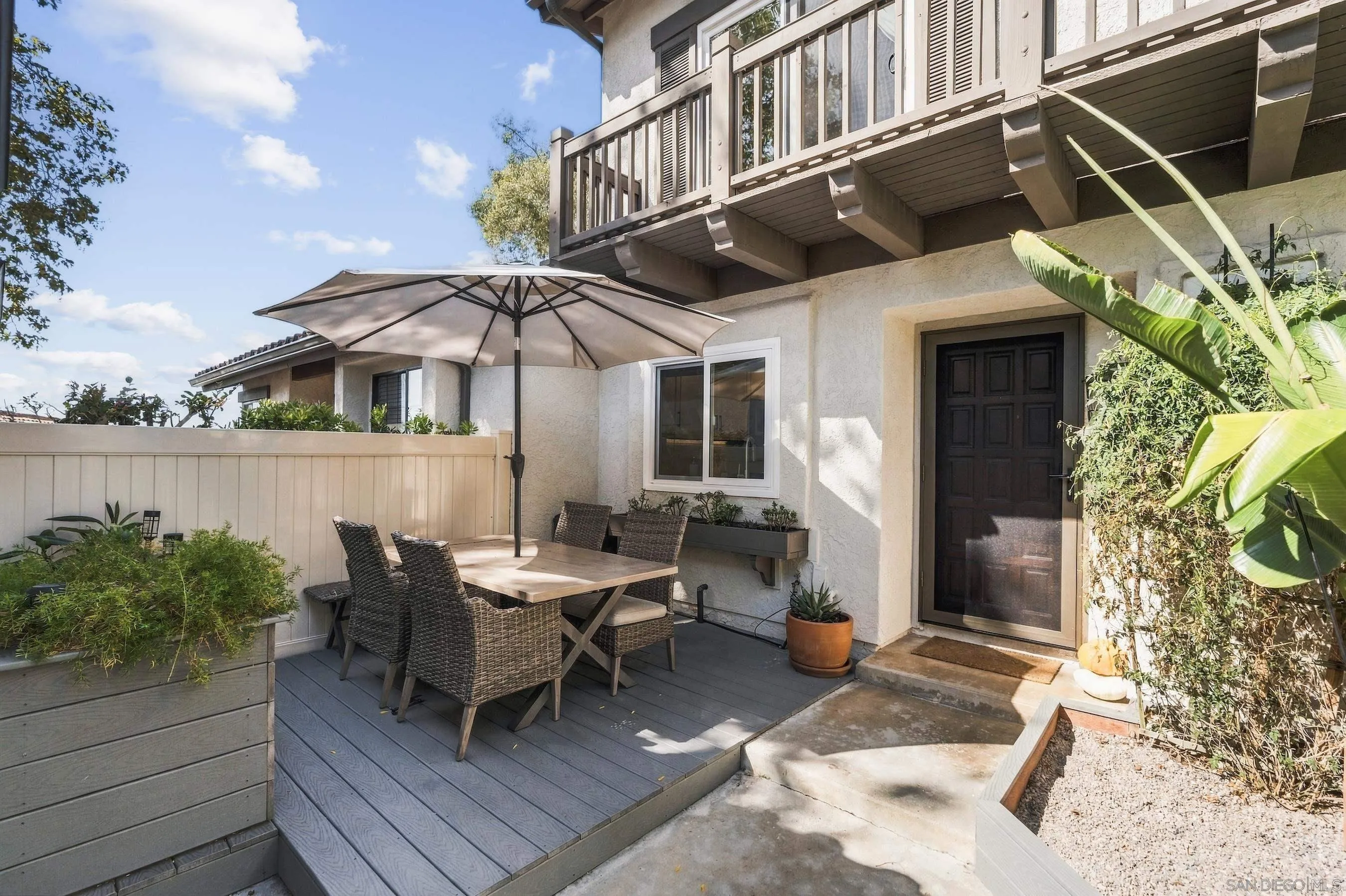Outdoor patio with a shaded wicker dining set, raised planters, and an overhanging balcony.