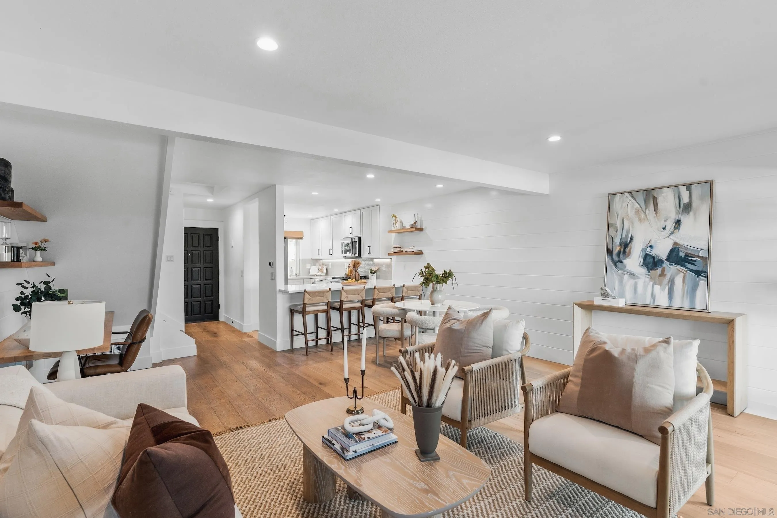 Open-plan living room and kitchen with white shiplap walls, wood floors, and neutral seating.