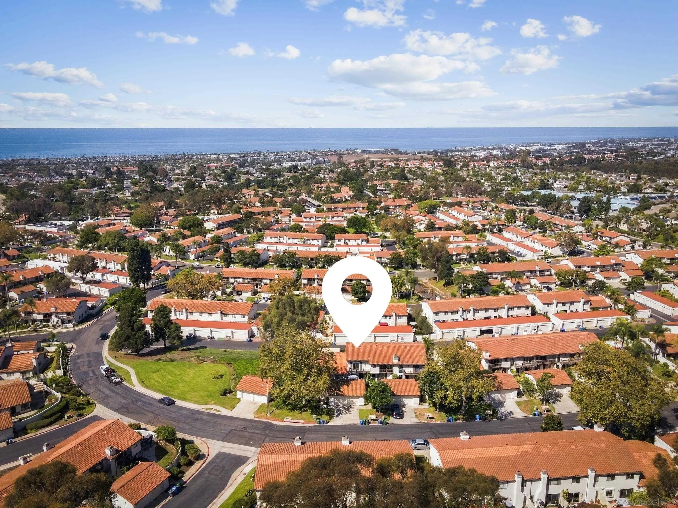 Aerial view of red-tile-roof homes near the coast, with a map pin marking one property.